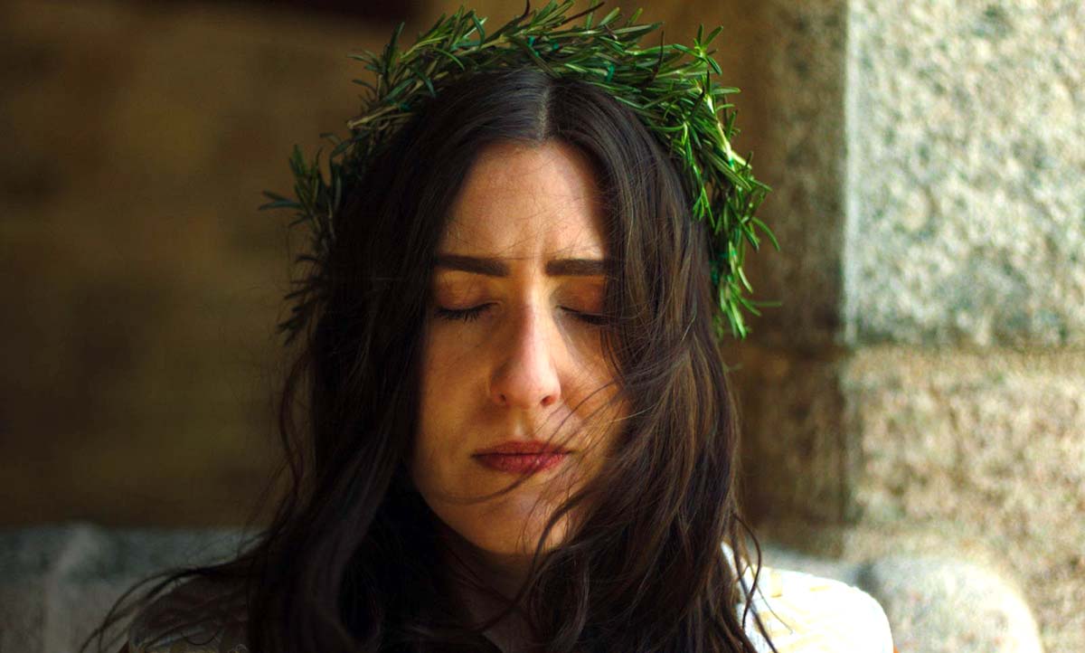 woman with long dark hair and crown of greenery, eyes closed in concentration