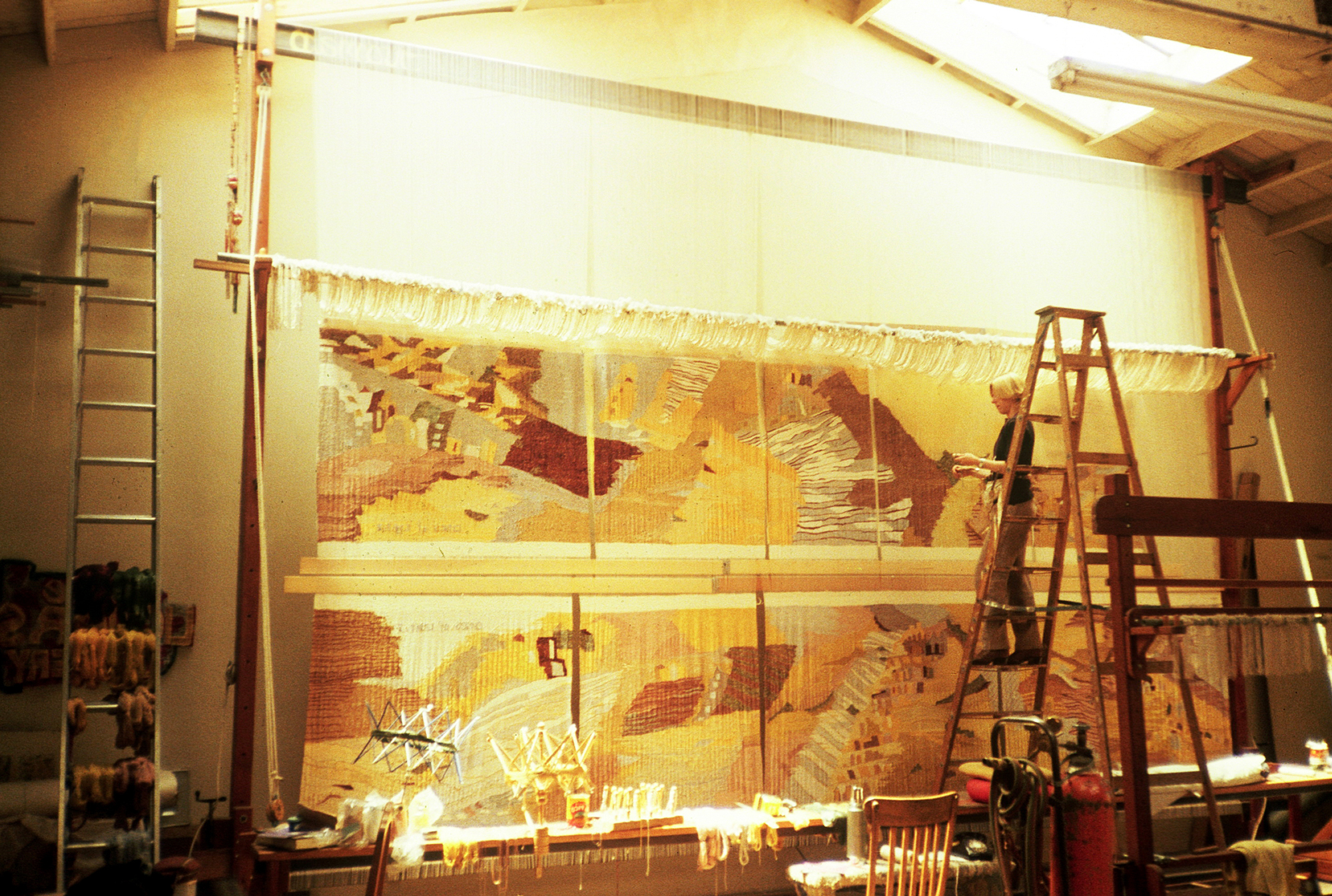 wide view of person on tall ladder in front of large tapestry in warehouse