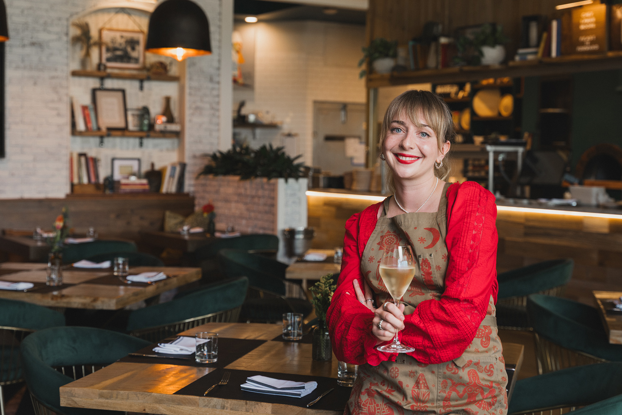 Portrait of a smiling chef holding a glass of white wine inside her restaurant.