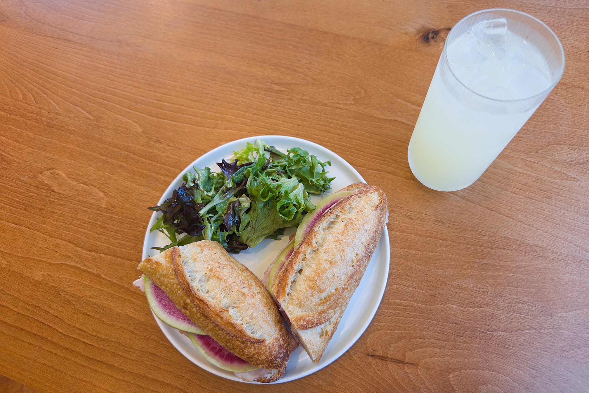 Overhead view of a baguette sandwich and a glass of lemonade.