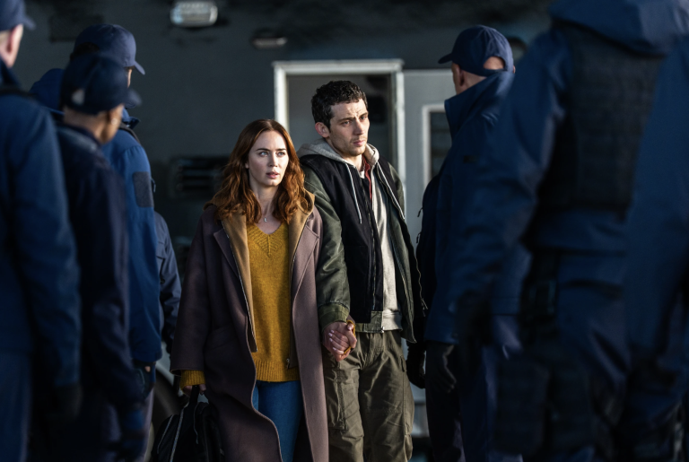 A white woman and white man hold hands tightly and move between two crowds of uniformed agents.