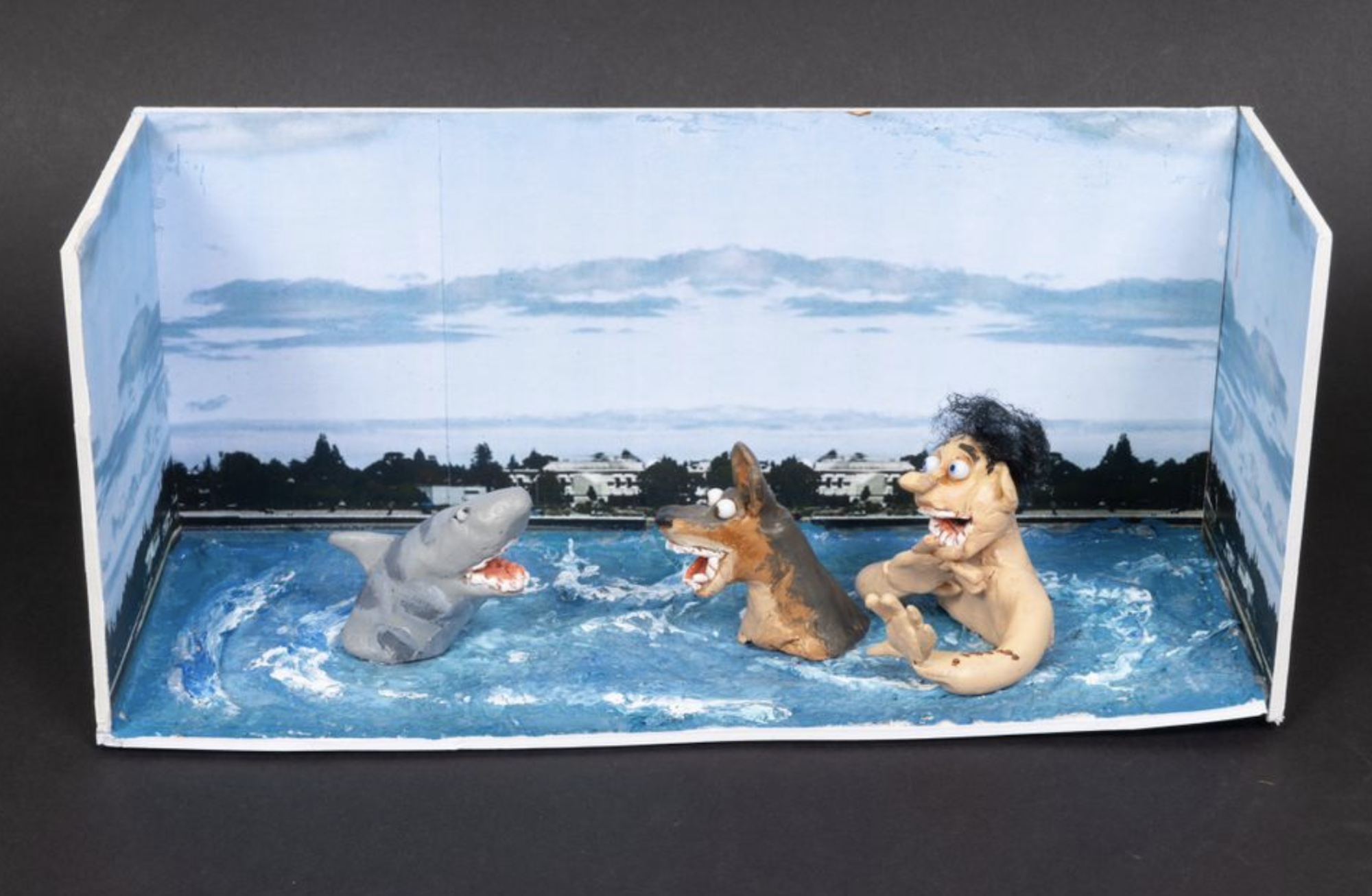 A model featuring a white boy and his dog, chest-deep in the ocean, facing off against a cartoonish-looking shark.