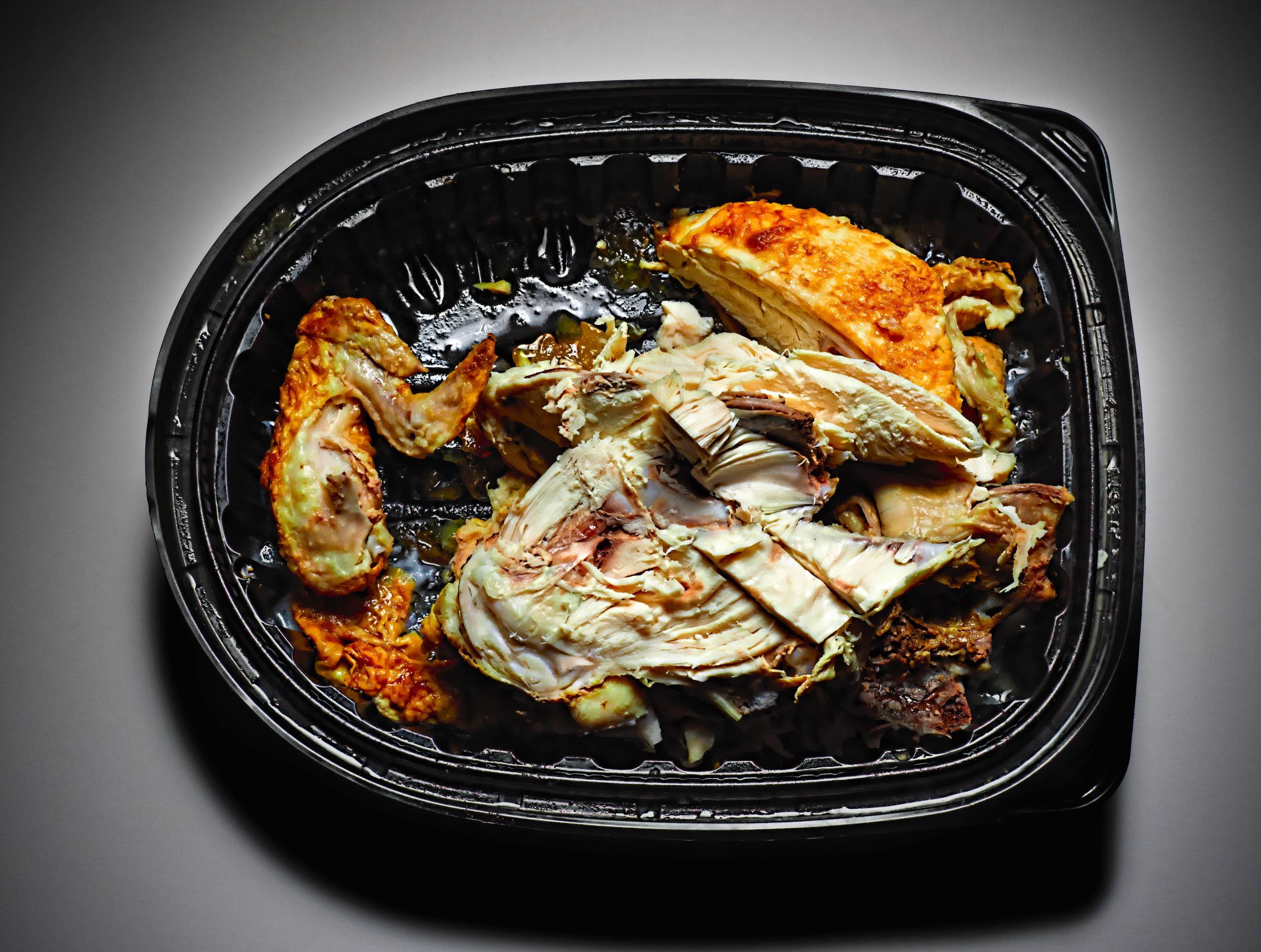 This photo shows a partially eaten chicken dish in a black plastic takeout container.