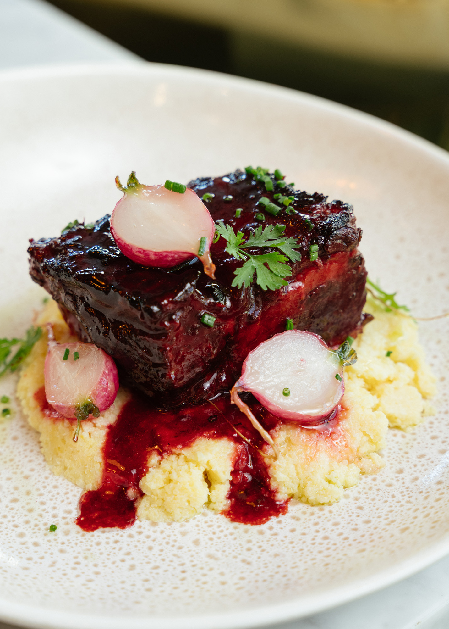 Purple braised short rib over a bed of polenta with sliced radishes sprinkled on top.