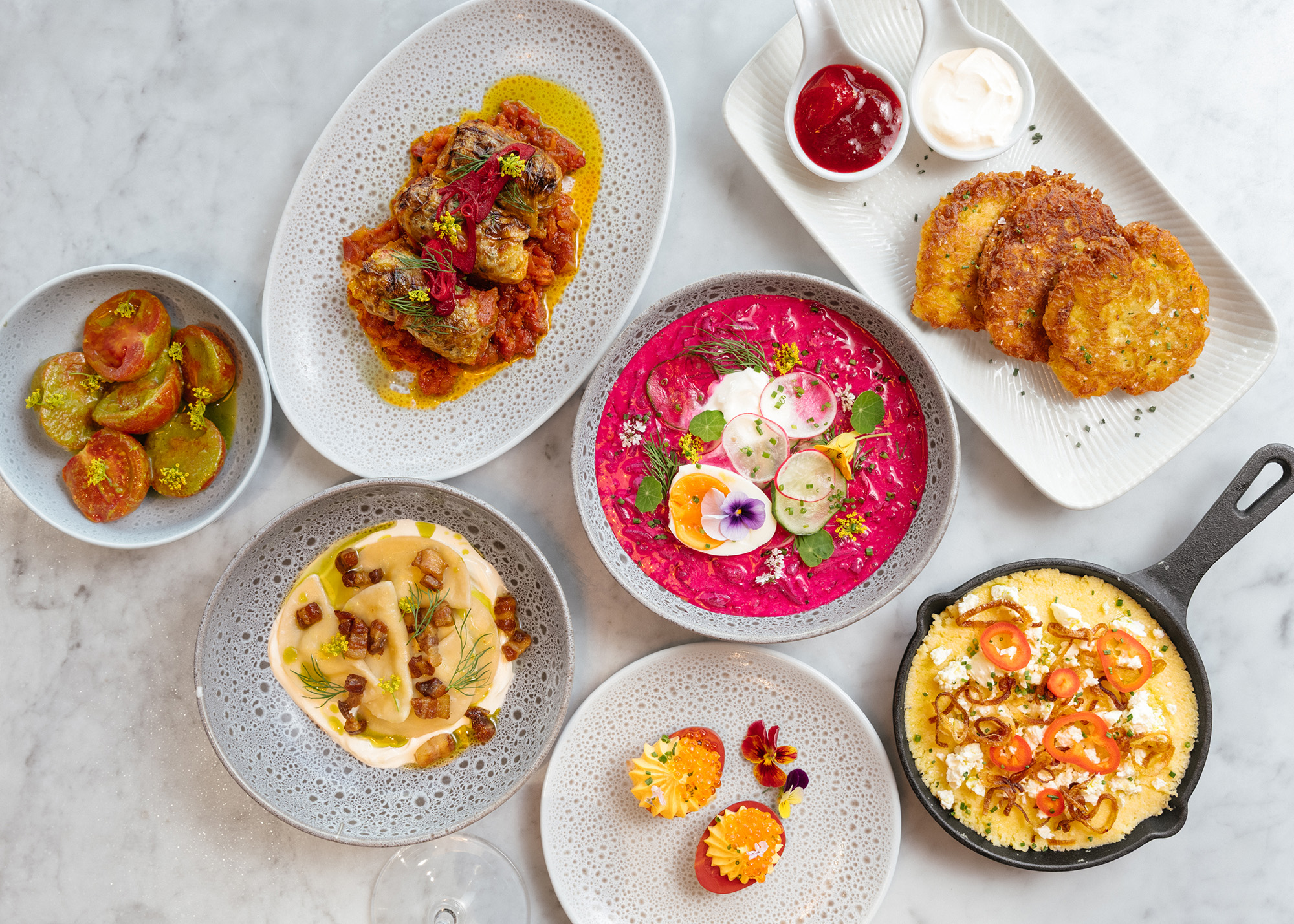 Overhead view of a spread of colorful Ukrainian dishes, including a bowl of bright pink borscht in the center.