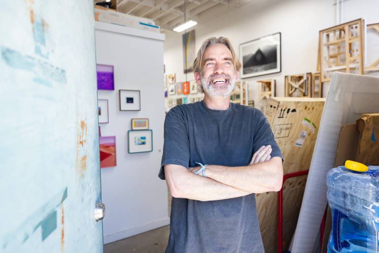 white man with gray hair smiles with arms crossed