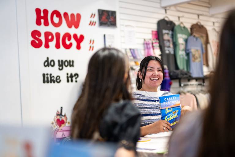 A woman laughs while holding up a book in front of a sign that says, "How spicy do you like it?"