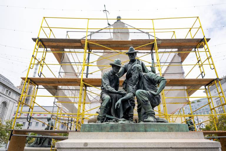 gold-covered scaffolding behind bronze statue of three miners