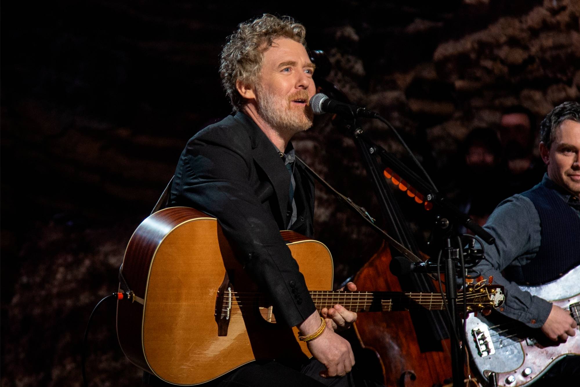 An irish man with an acoustic guitar looks to the right wile singing