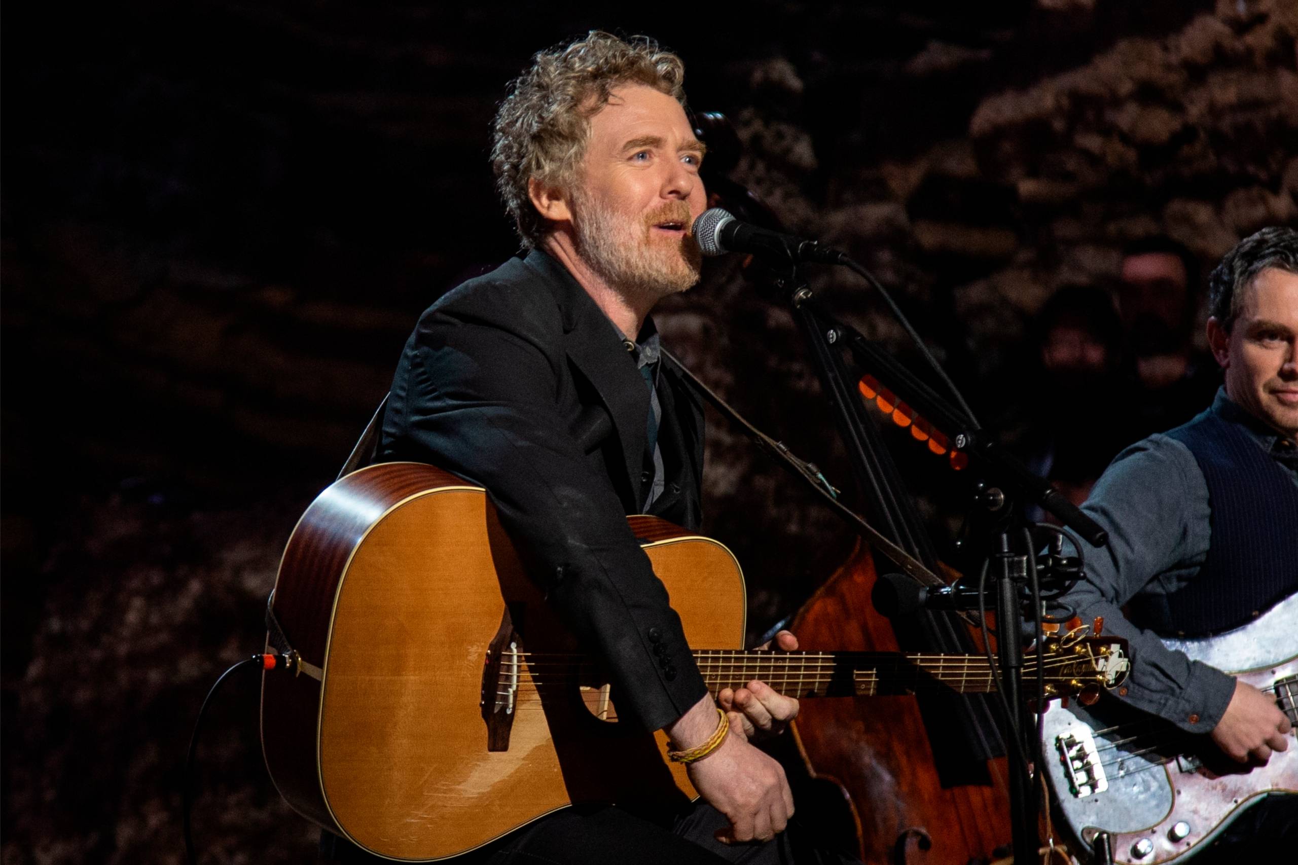 An irish man with an acoustic guitar looks to the right wile singing