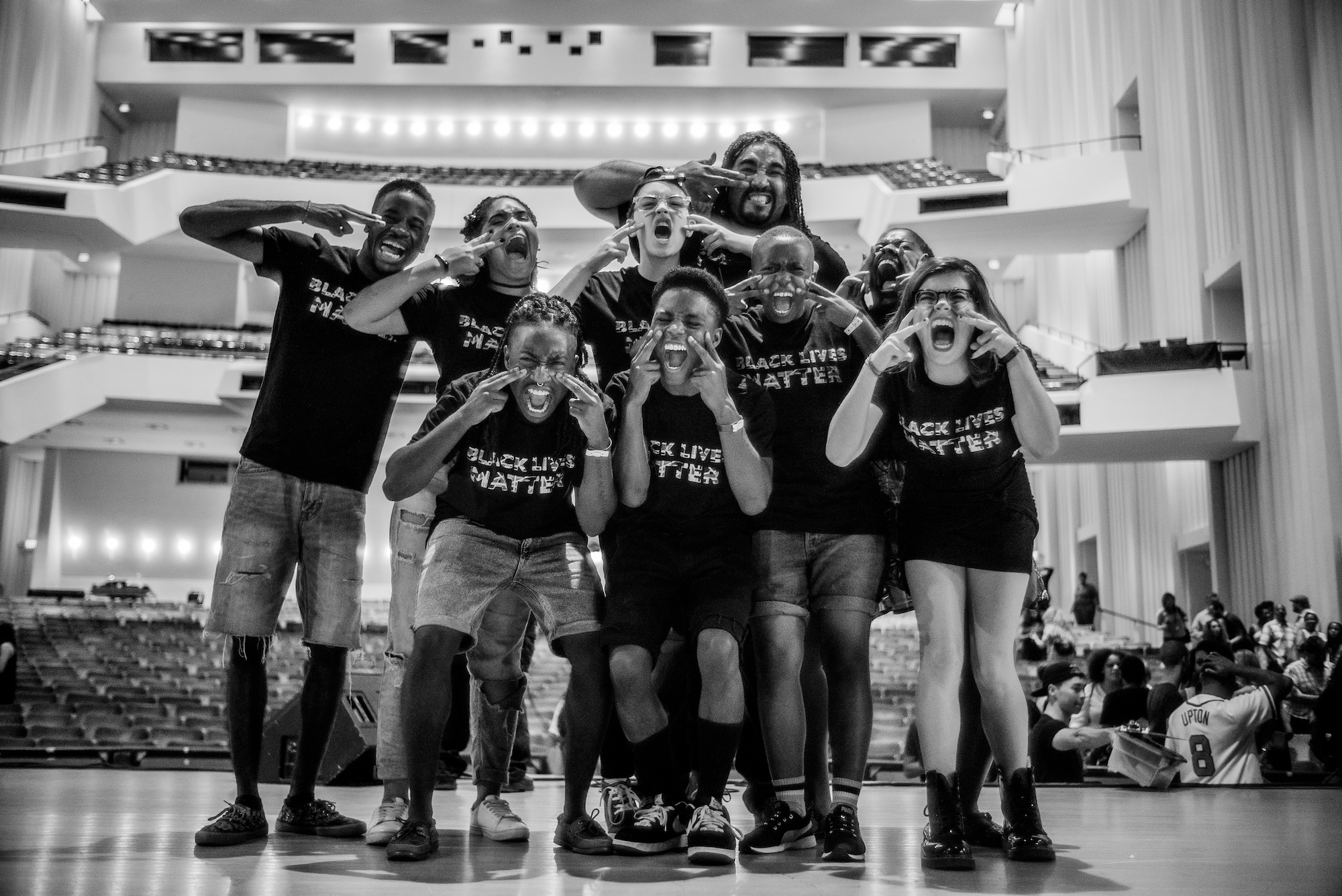 A black and white image of a group of people standing on stage, posing and taking a photo.