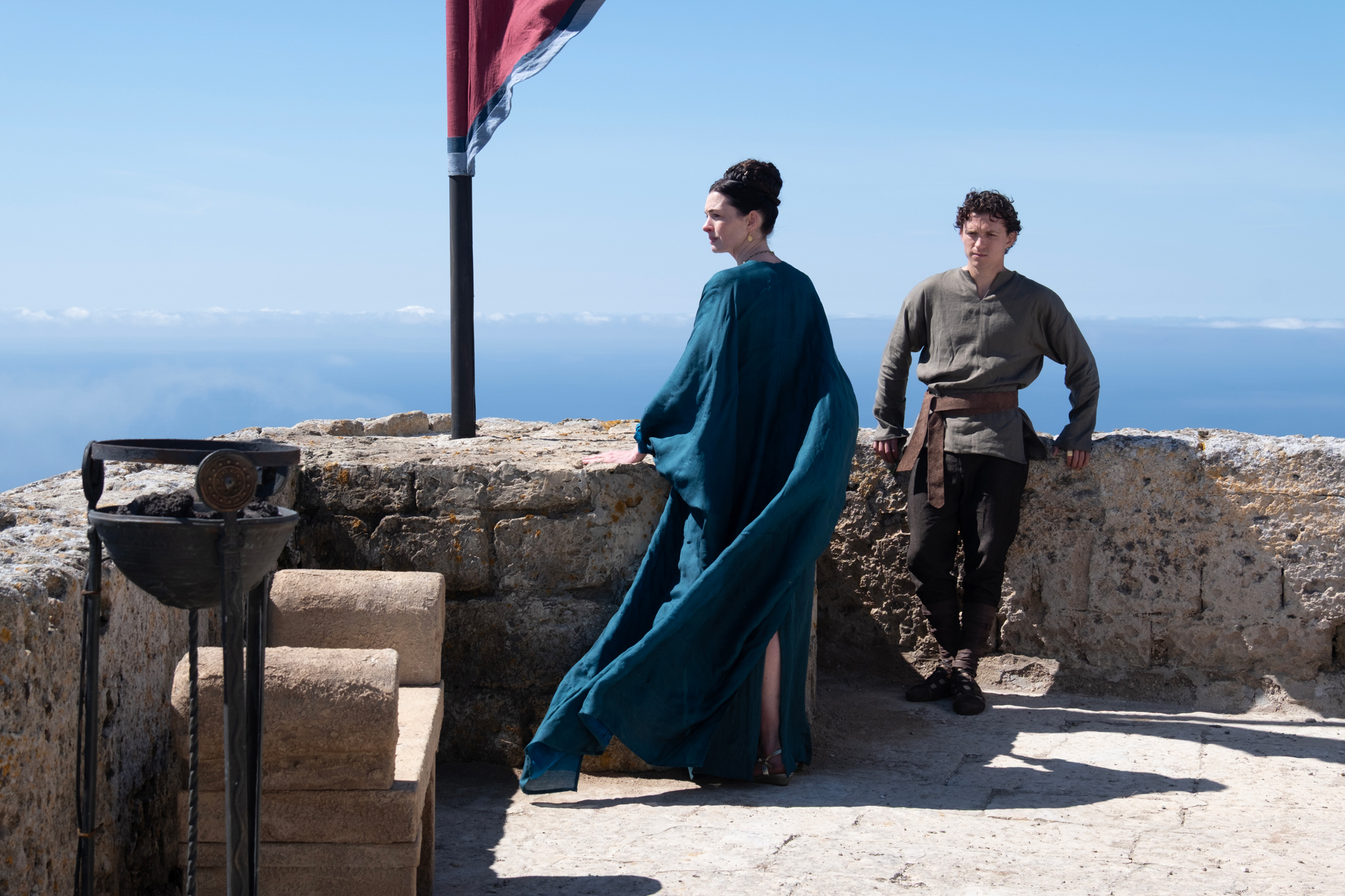 woman in blue robe and younger man stand looking out from parapet to distance
