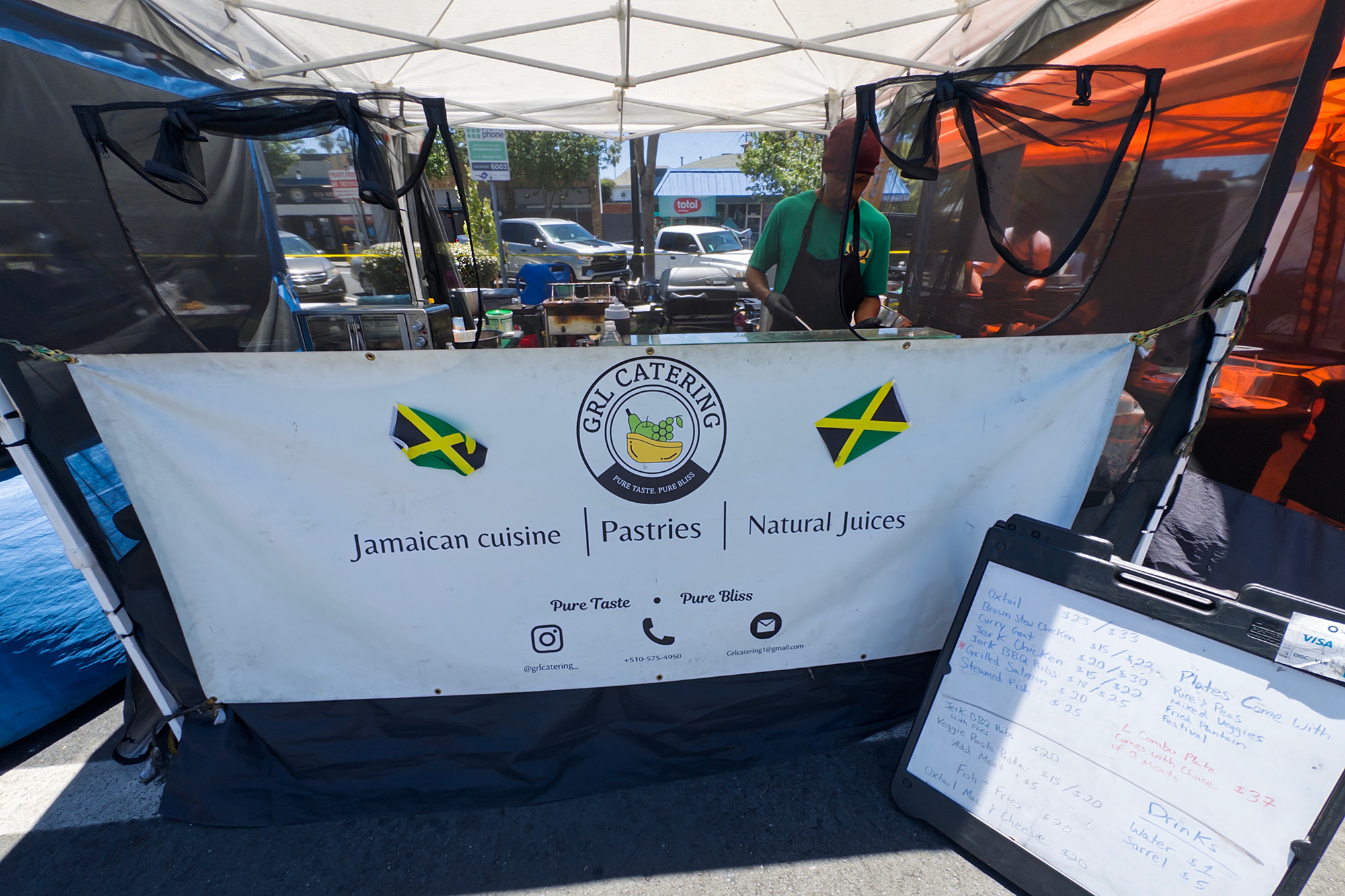 A man serving food inside a food tent. The name of the stand is "GRL Catering."
