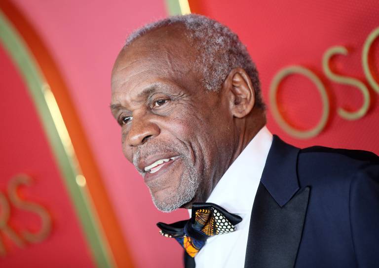 An older Black man in a bowtie and formalwear, against a red and muava background