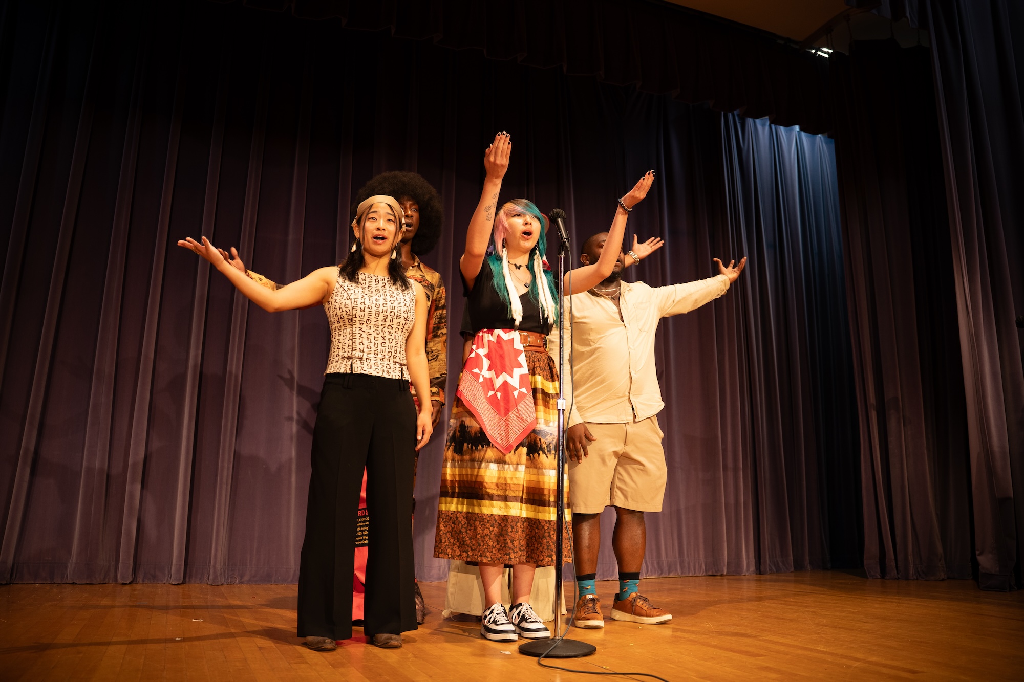Four poets making hand gestures while performing on stage.