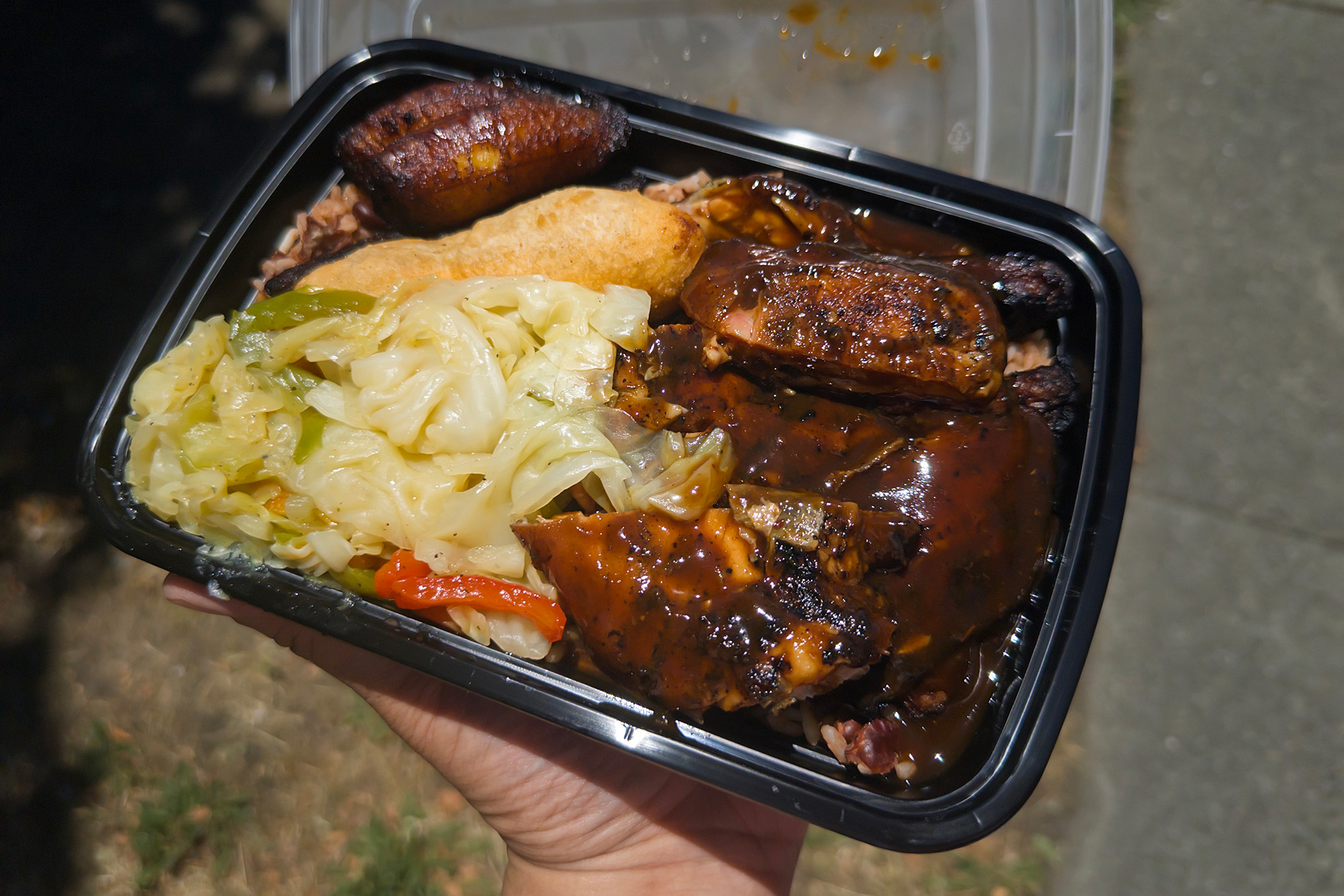 Jerk chicken, cabbage and plantains in a takeout container.