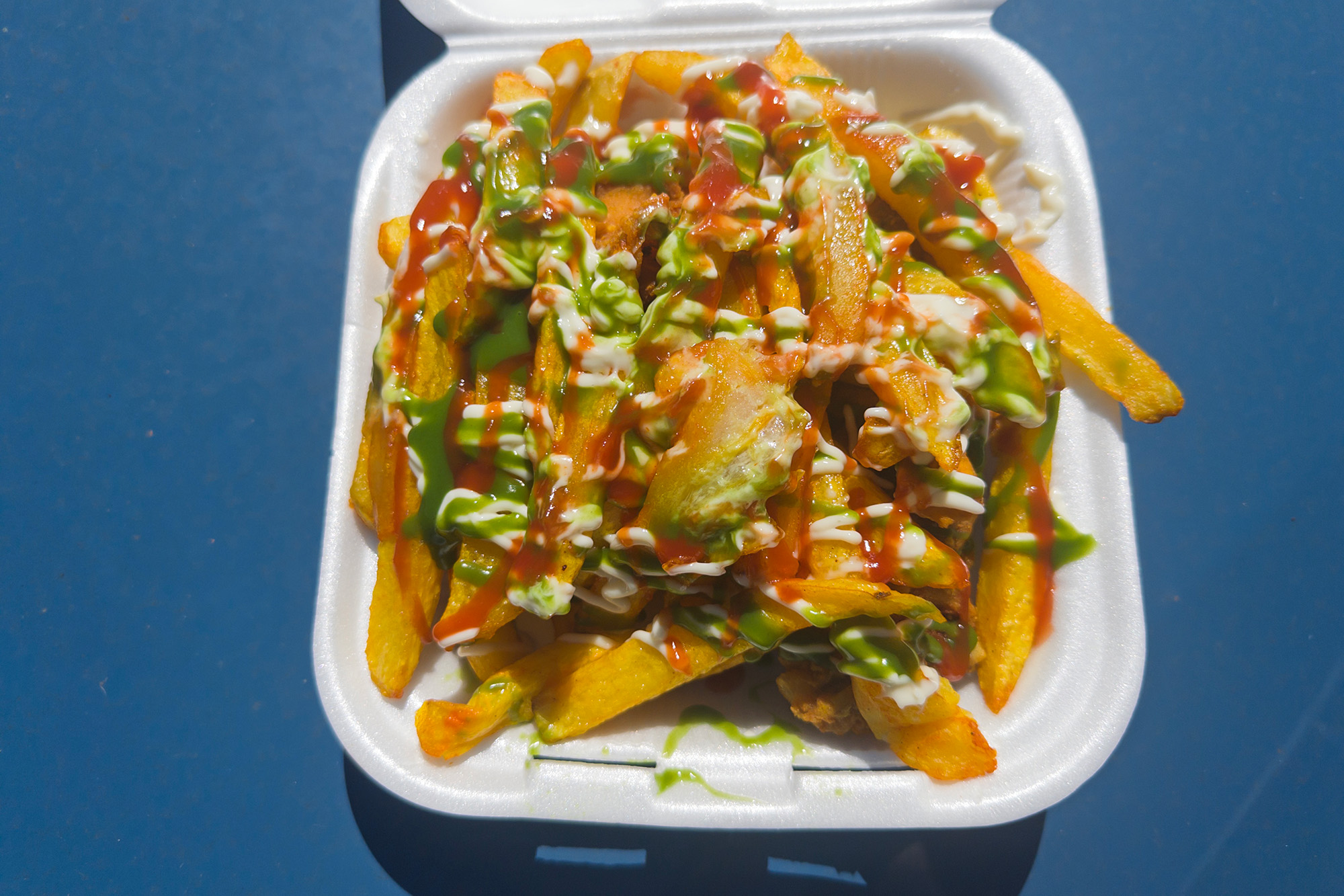 A huge mound of sauce-drizzled fries in a Styrofoam clamshell container.