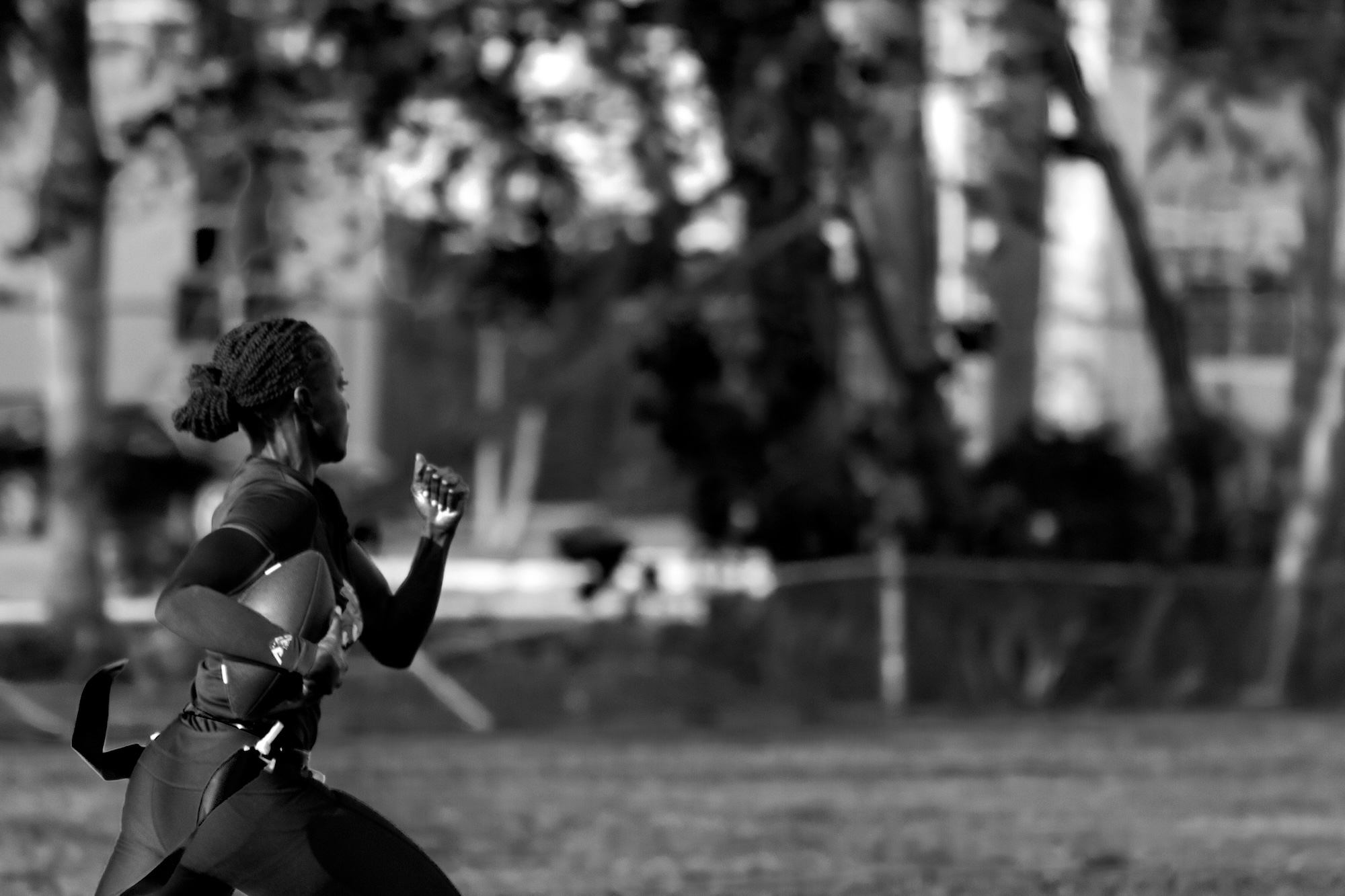 A wide photograph of a Black female flag football player sprinting with the ball under her right arm.