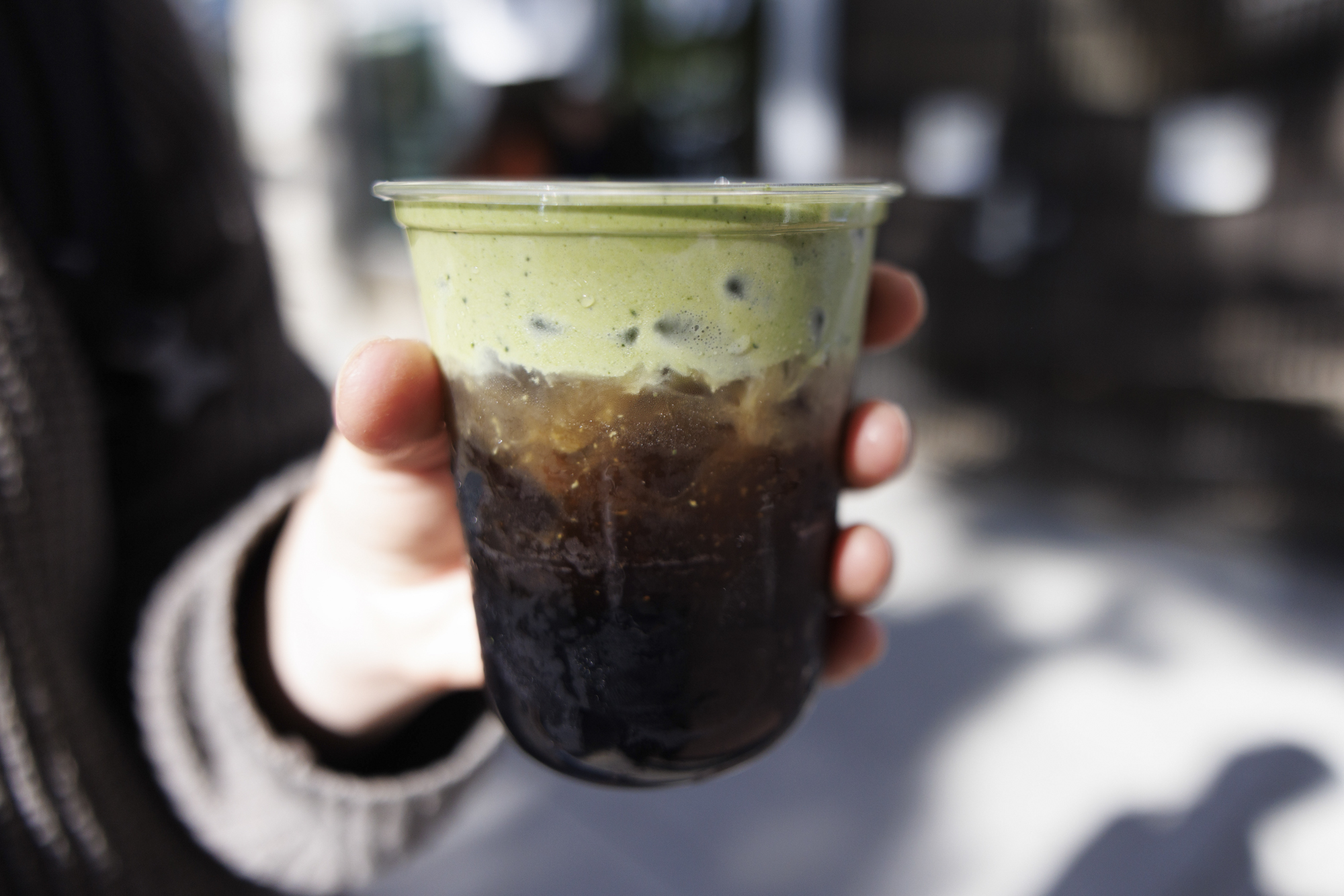Hand holding a cup of iced coffee topped with a layer of pale green matcha cream.