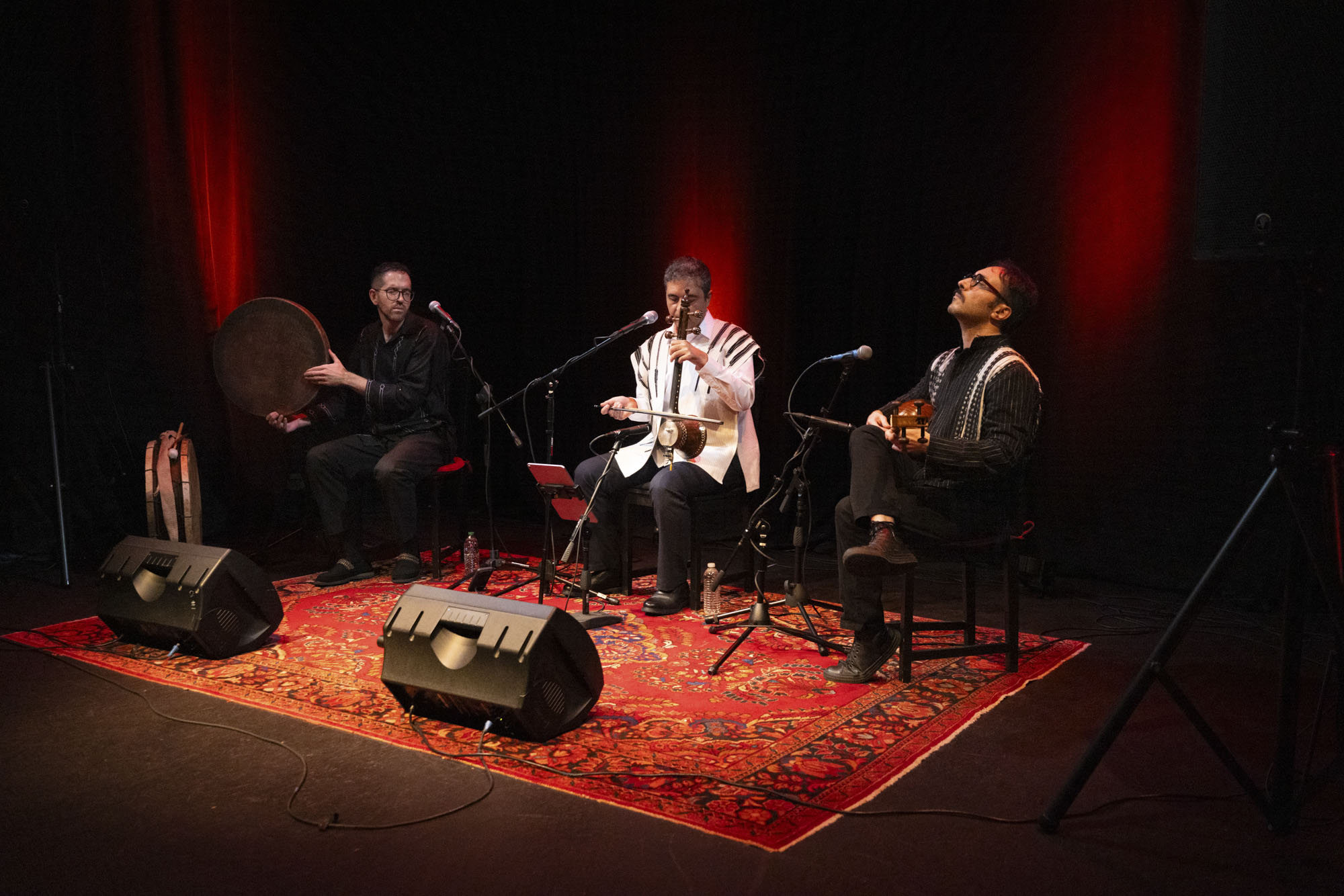 Three musicians on stage play traditional Iranian percussion and string instruments.
