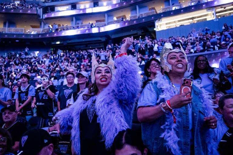 two women in headdresses cheer in stadium with blue and purple light