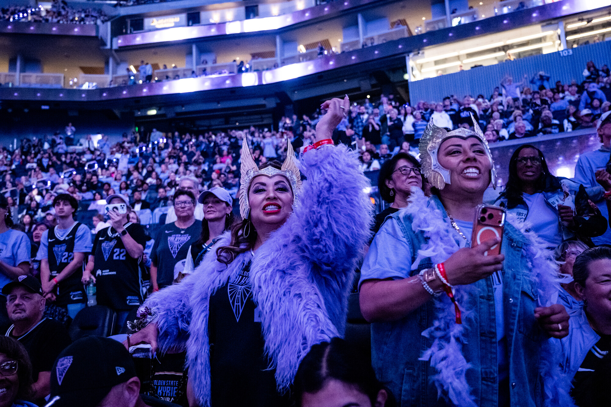 two women in headdresses cheer in stadium with blue and purple light