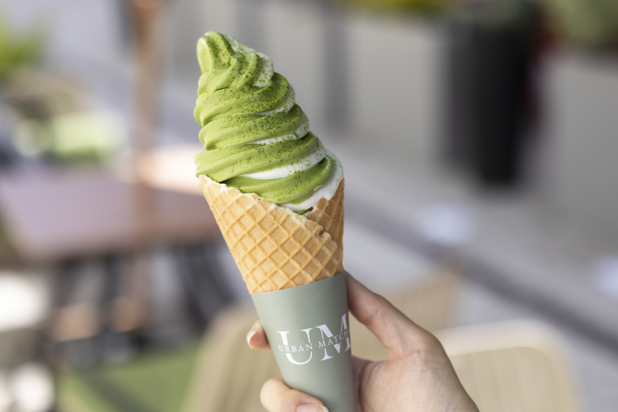 Hand holding matcha soft serve ice cream on a sugar cone.