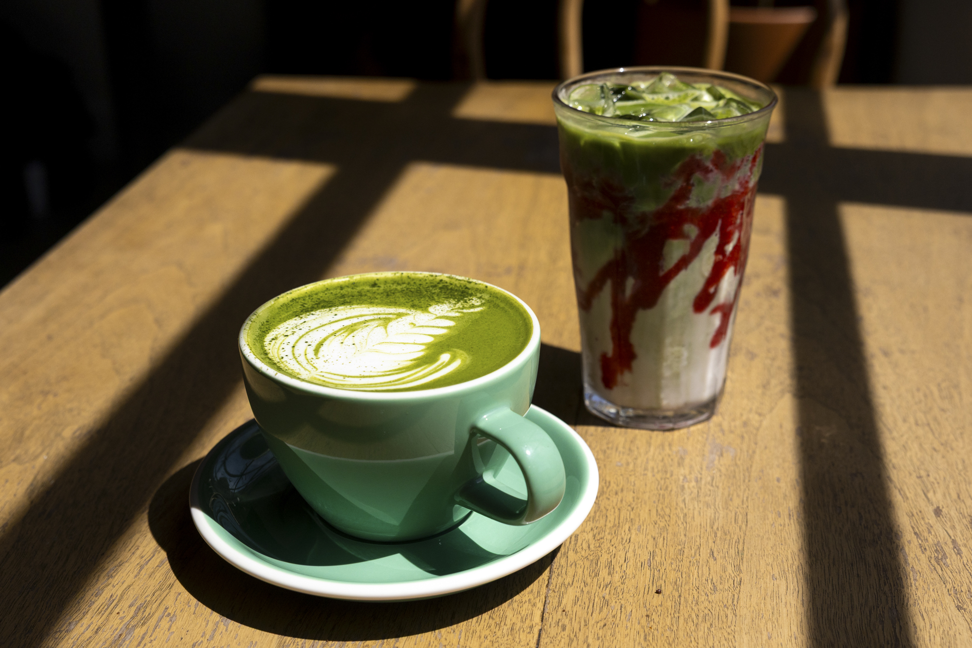 Matcha latte and strawberry matcha latte on a sun-dappled wooden table.