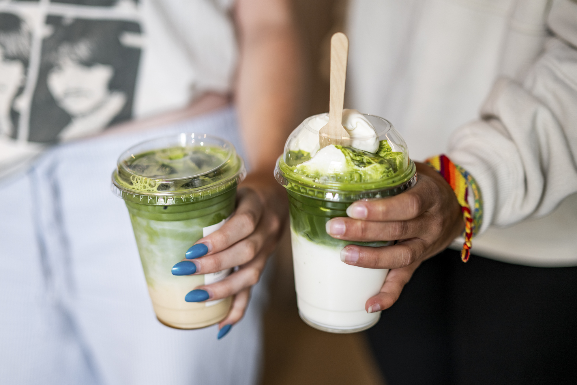 Two customers side by side holding creamy matcha drinks.