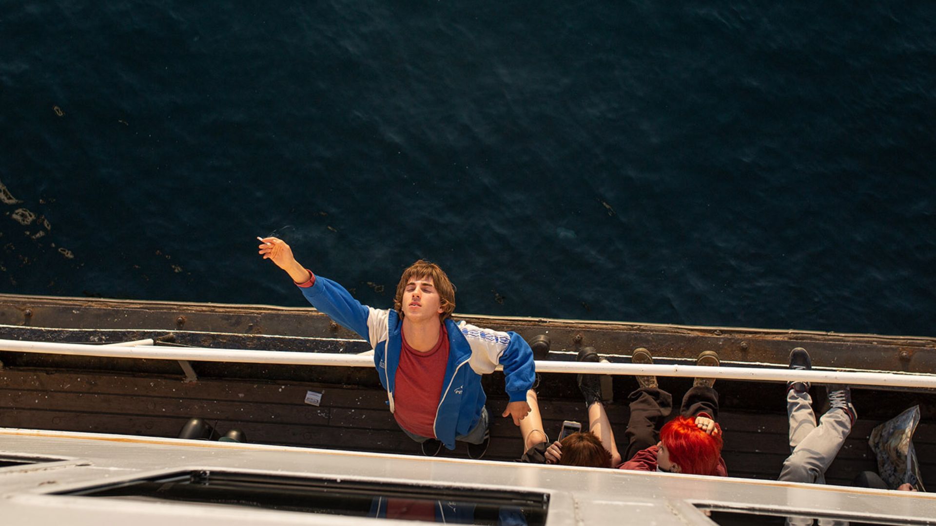 young man leans back against ferry railing with eyes closed and cigarette in hand