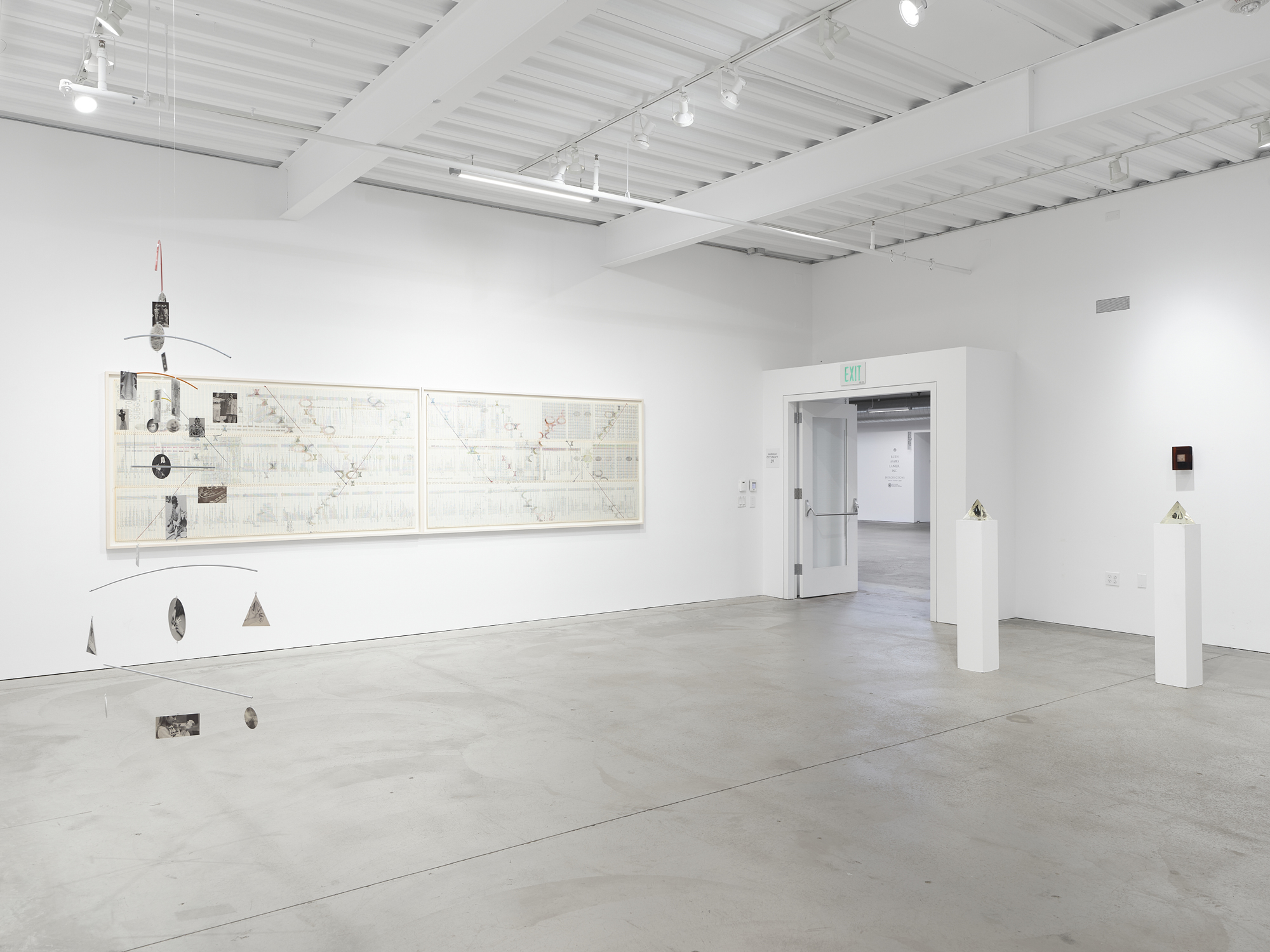 gallery view with mobile, wide framed work on paper and small sculptures on narrow pedestals