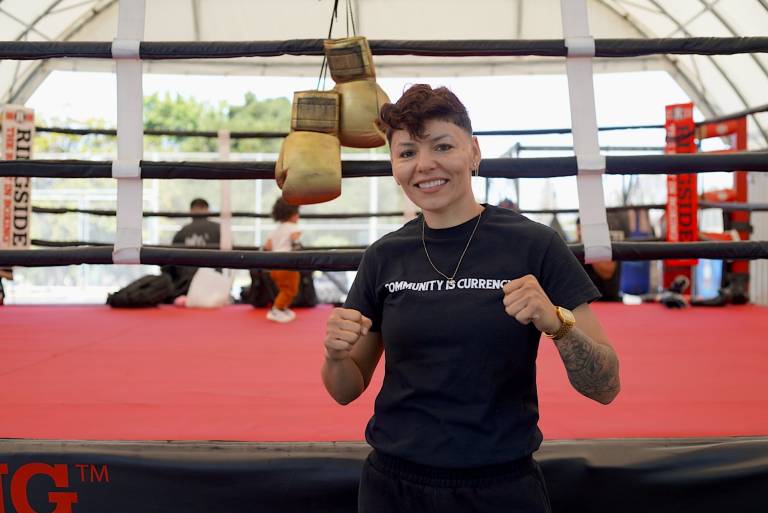 A woman posing for a photo in front of a boxing ring.