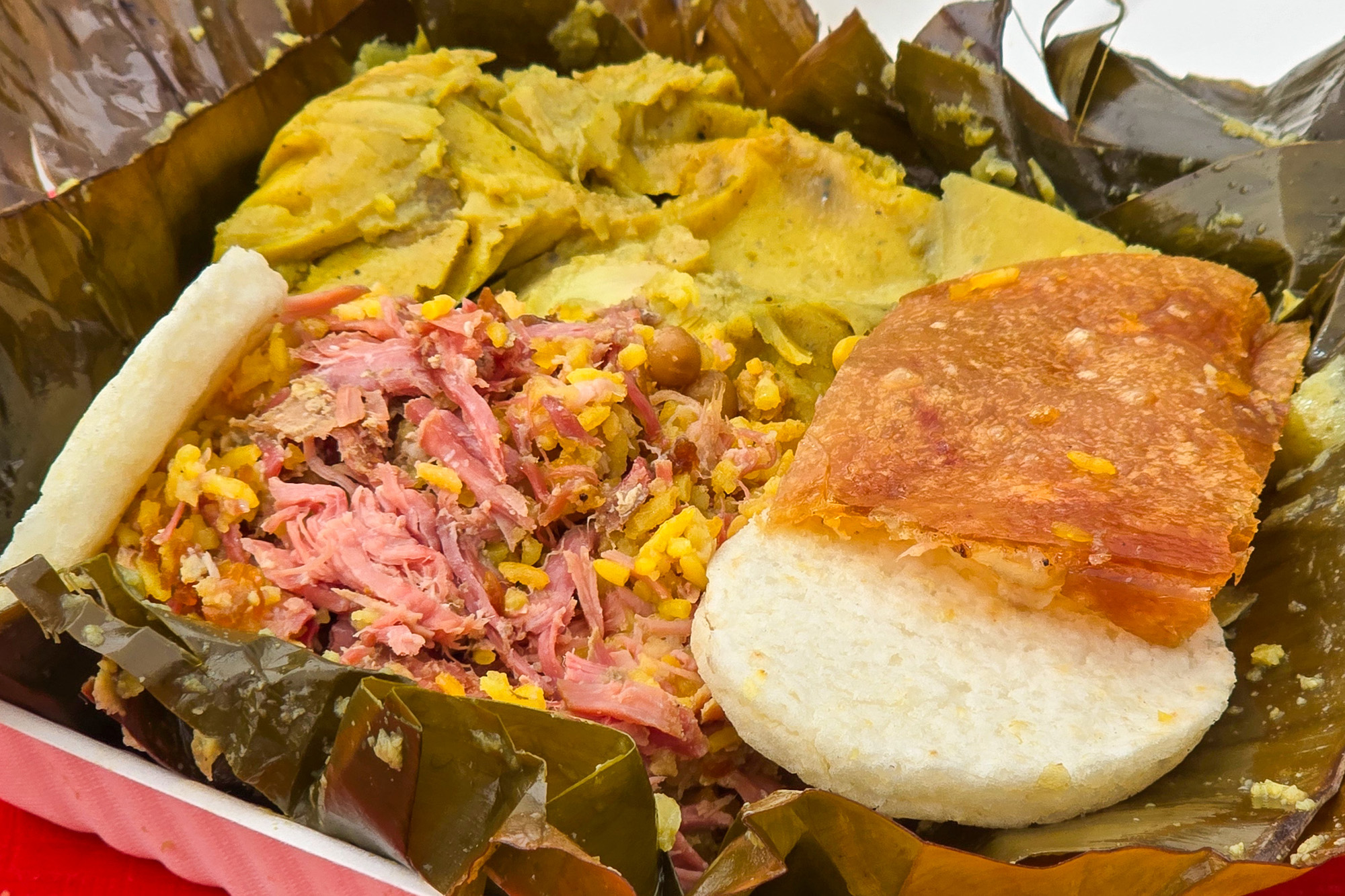 An unwrapped tamal topped with meat and a shard of crispy pork skin.