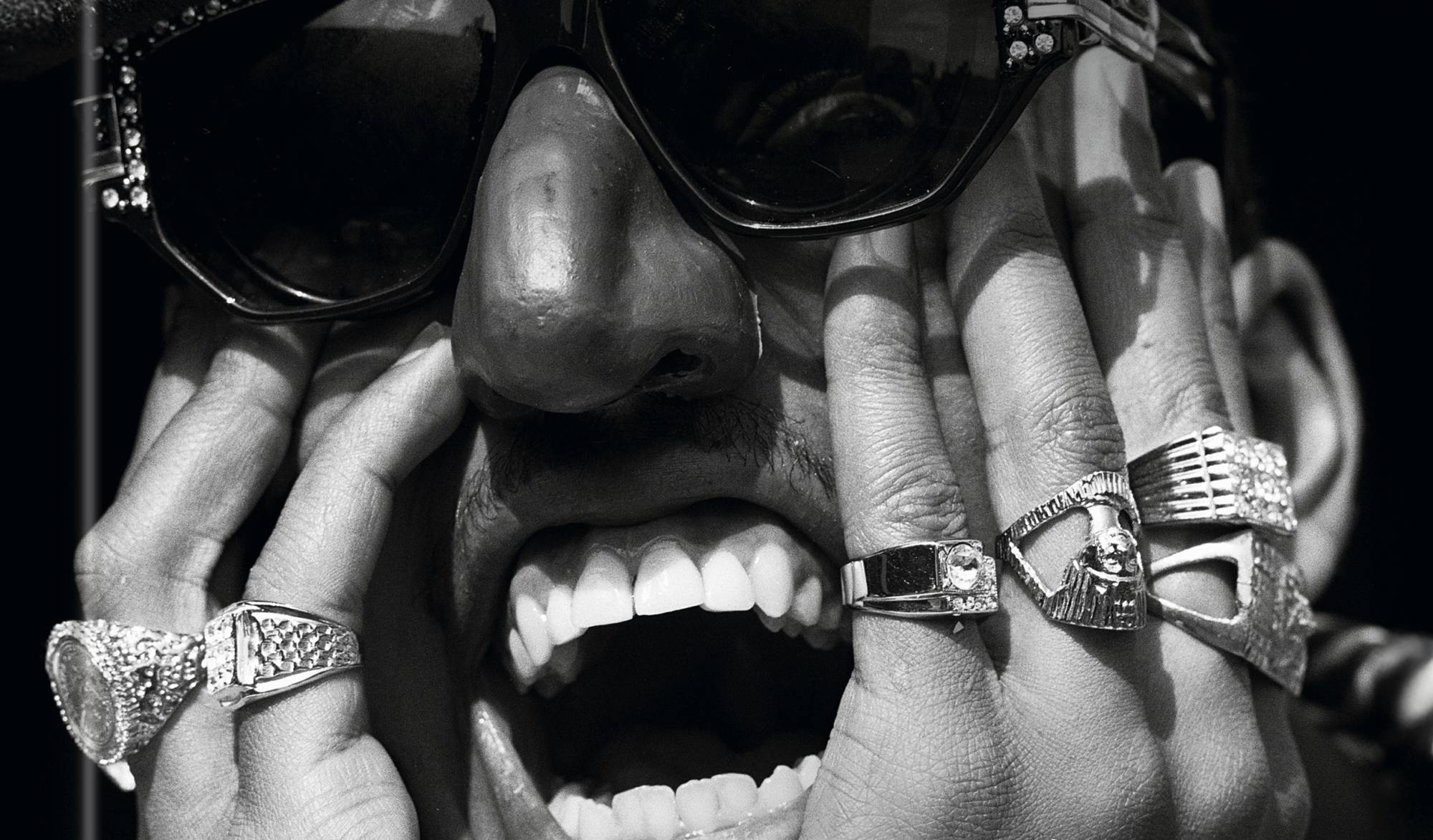 A close-up on a Black man's face, wearing a Groucho Marx style novelty mask with glasses and a big nose, his hands on his cheeks