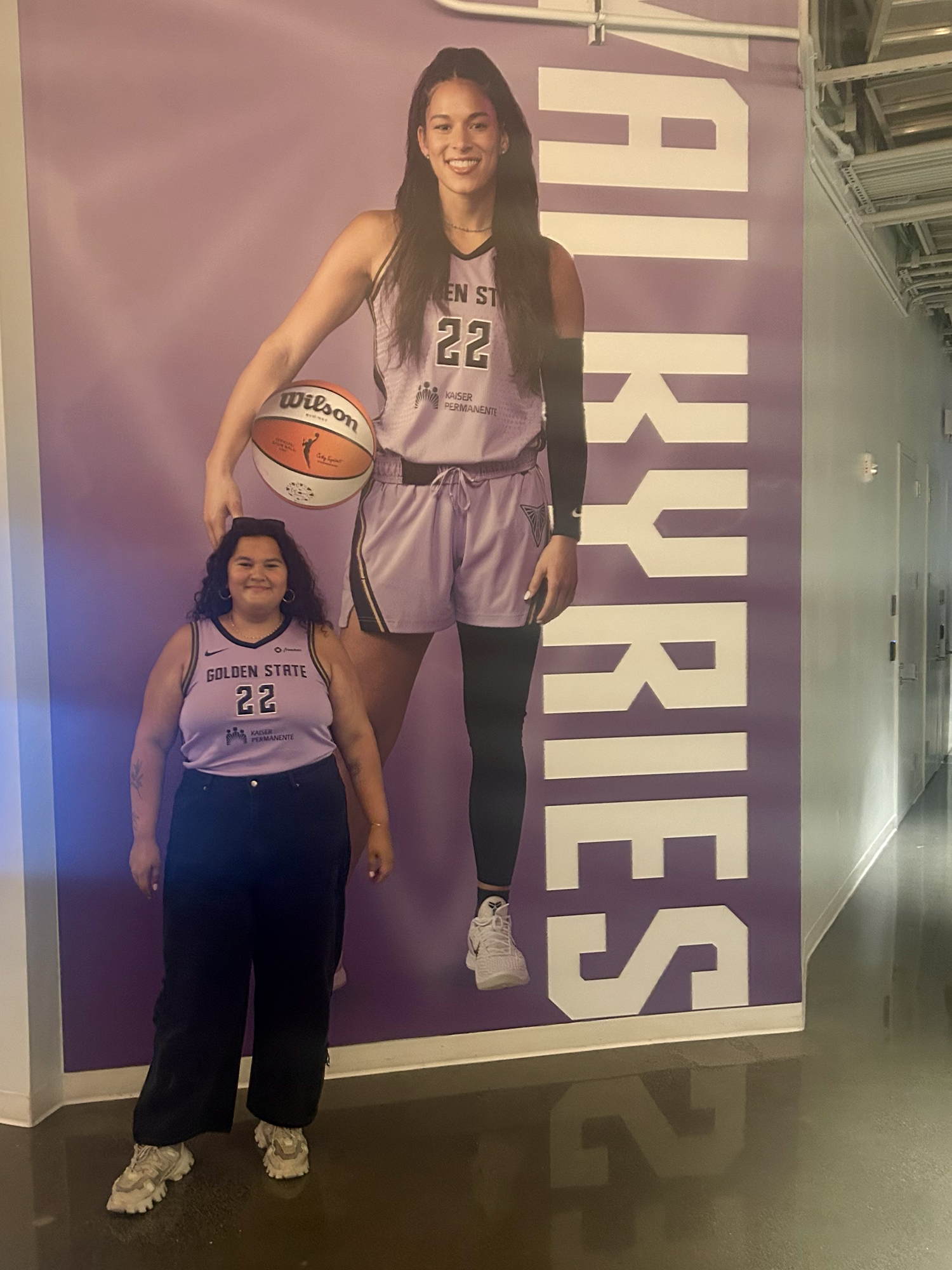 smiling person with long dark hair in violet sports jersey in front of giant poster of athlete in same uniform