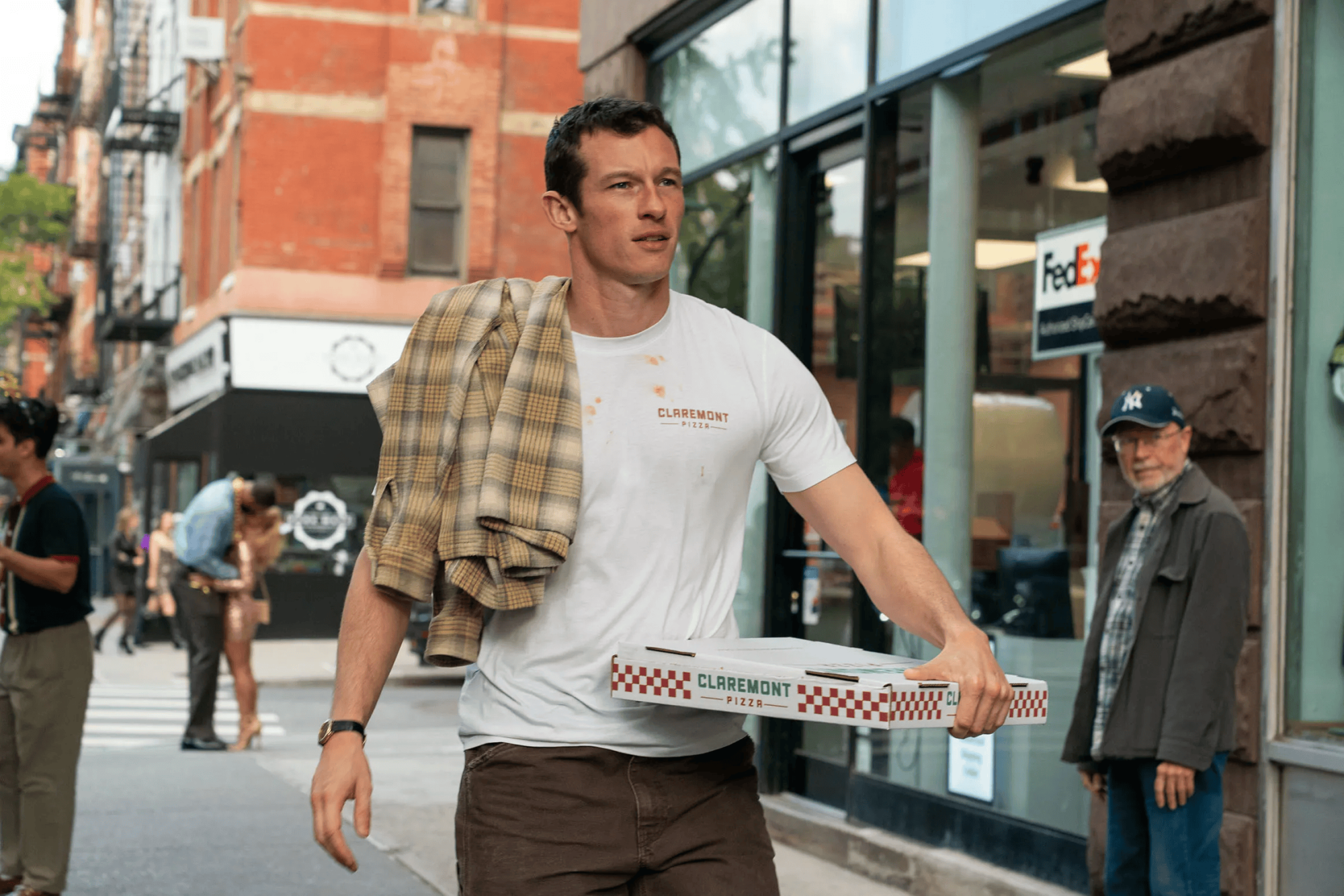A man holds a large pizza box on the sidewalk.