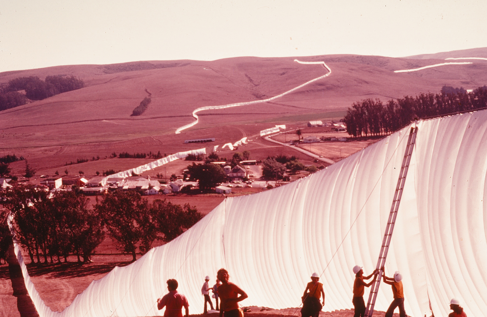 red-tinged image of crew raising tall fabric fence with trail of it in distance