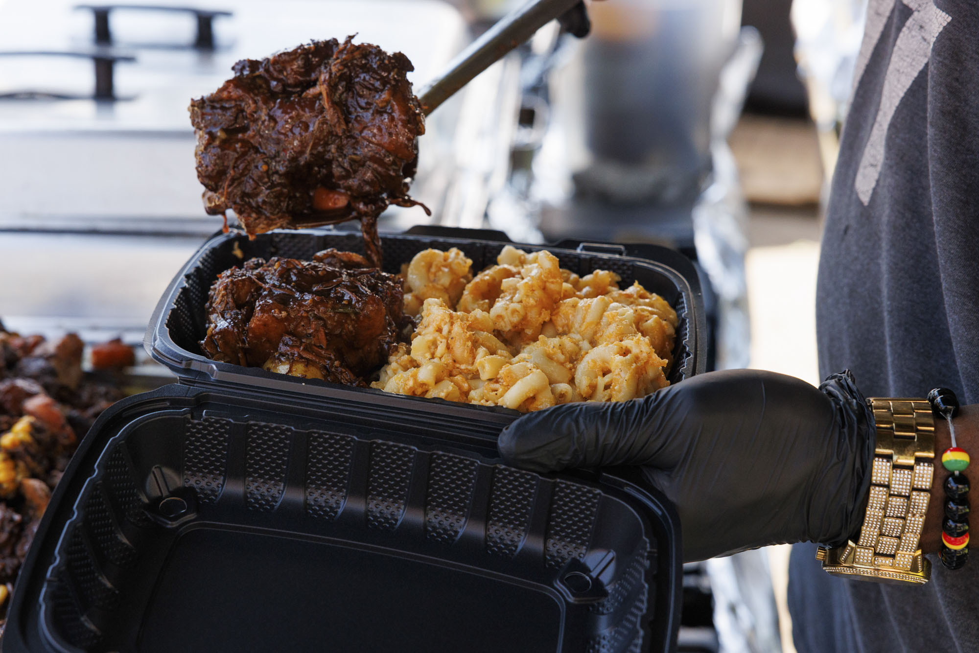 Man scooping jerk oxtails into a takeout container.