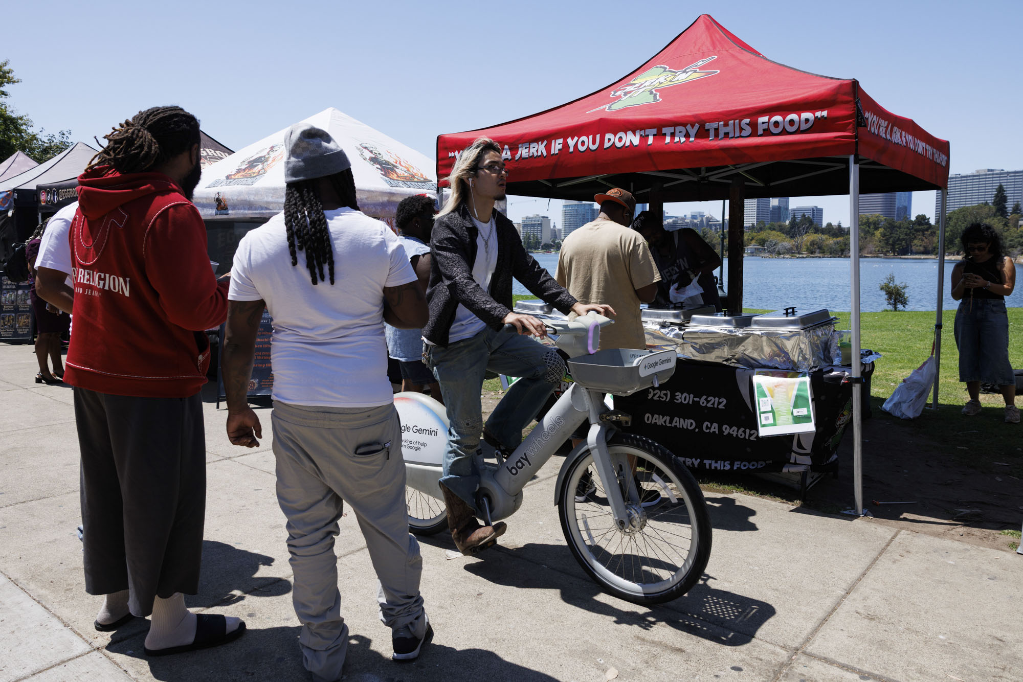 Customers and passersby stand in front of a lakeside food tent.