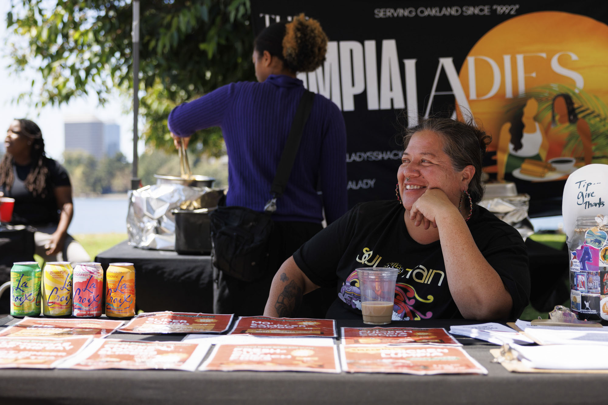 A woman seated inside her food tent. The sign behind her reads, "Lumpia Ladies."