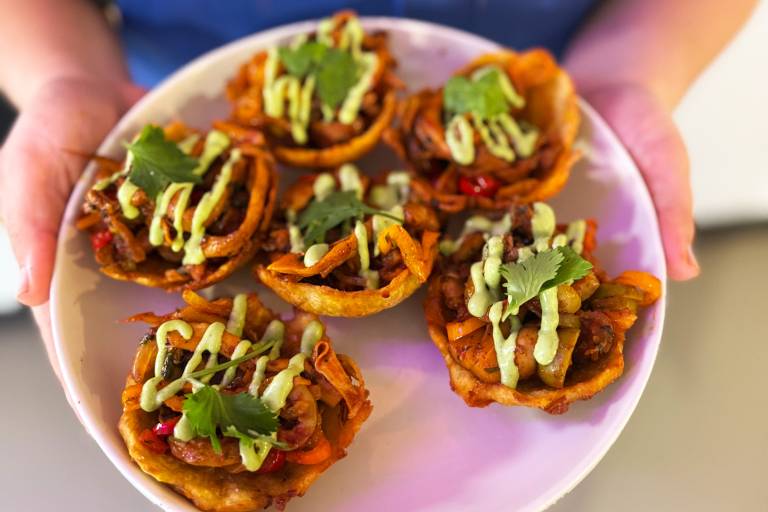 Hands holding a plate of loaded Panamanian patacones (fried green plantains).