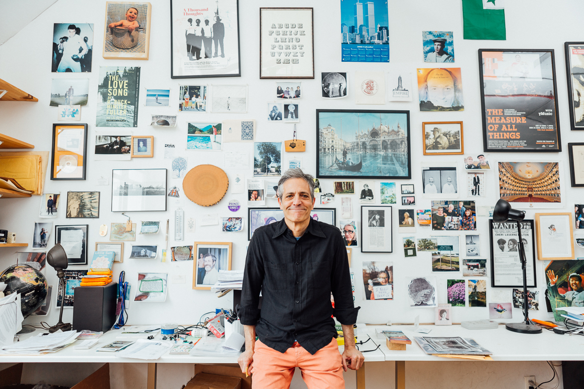 white man with gray hair smiles in front of wall covered in movie posters and photographs