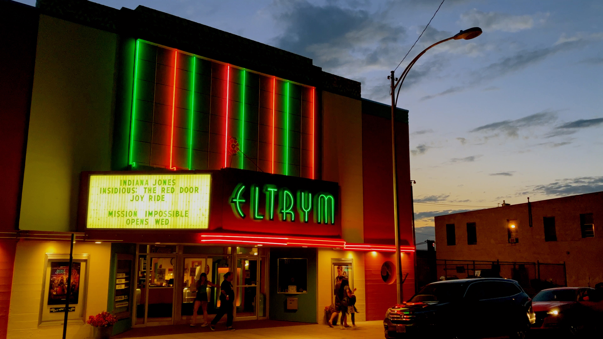 neon sign and marquee of small theater against sky with sunset