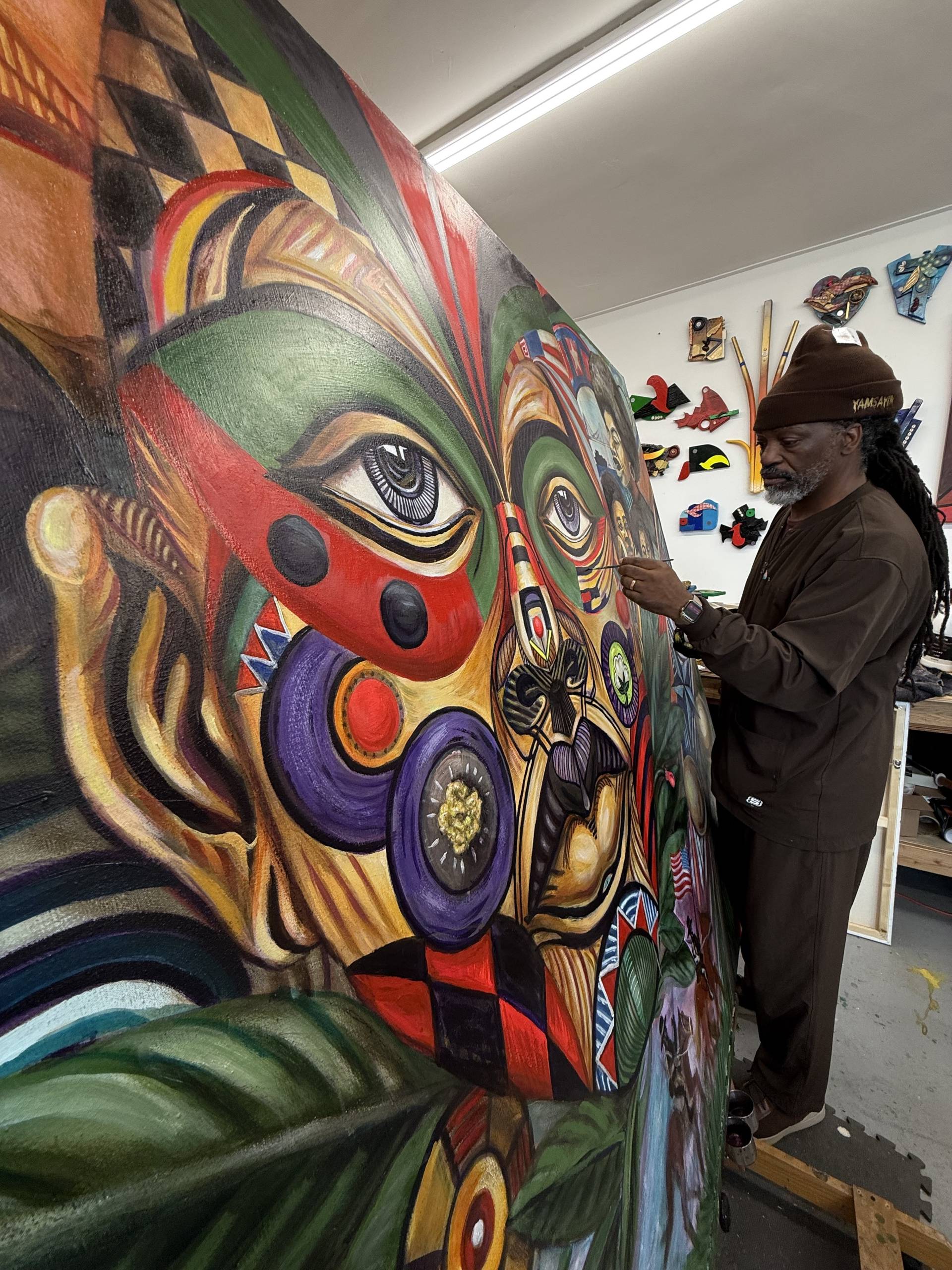 An African American man in a brown outfit panting a giant colorful mural.