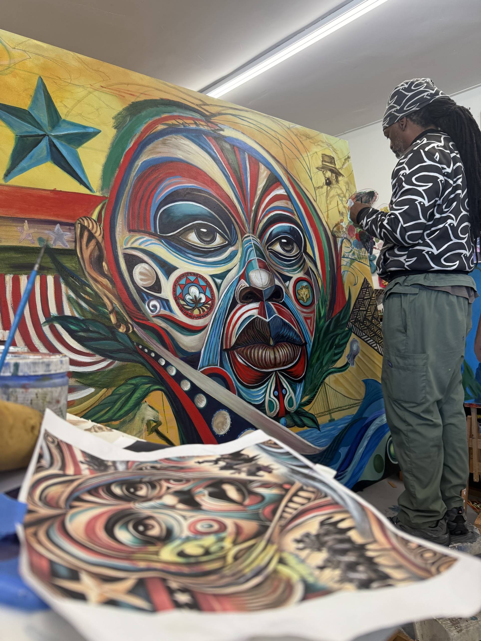 A man faces a colorful canvas as he paints in a studio.