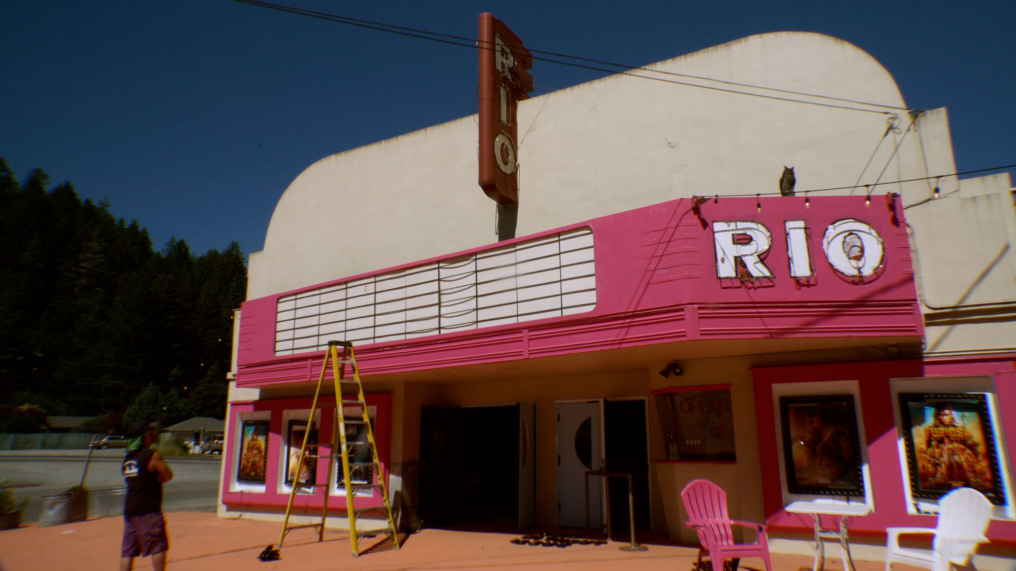 man stands in front of empty marquee on pink façade of quonset hut theater