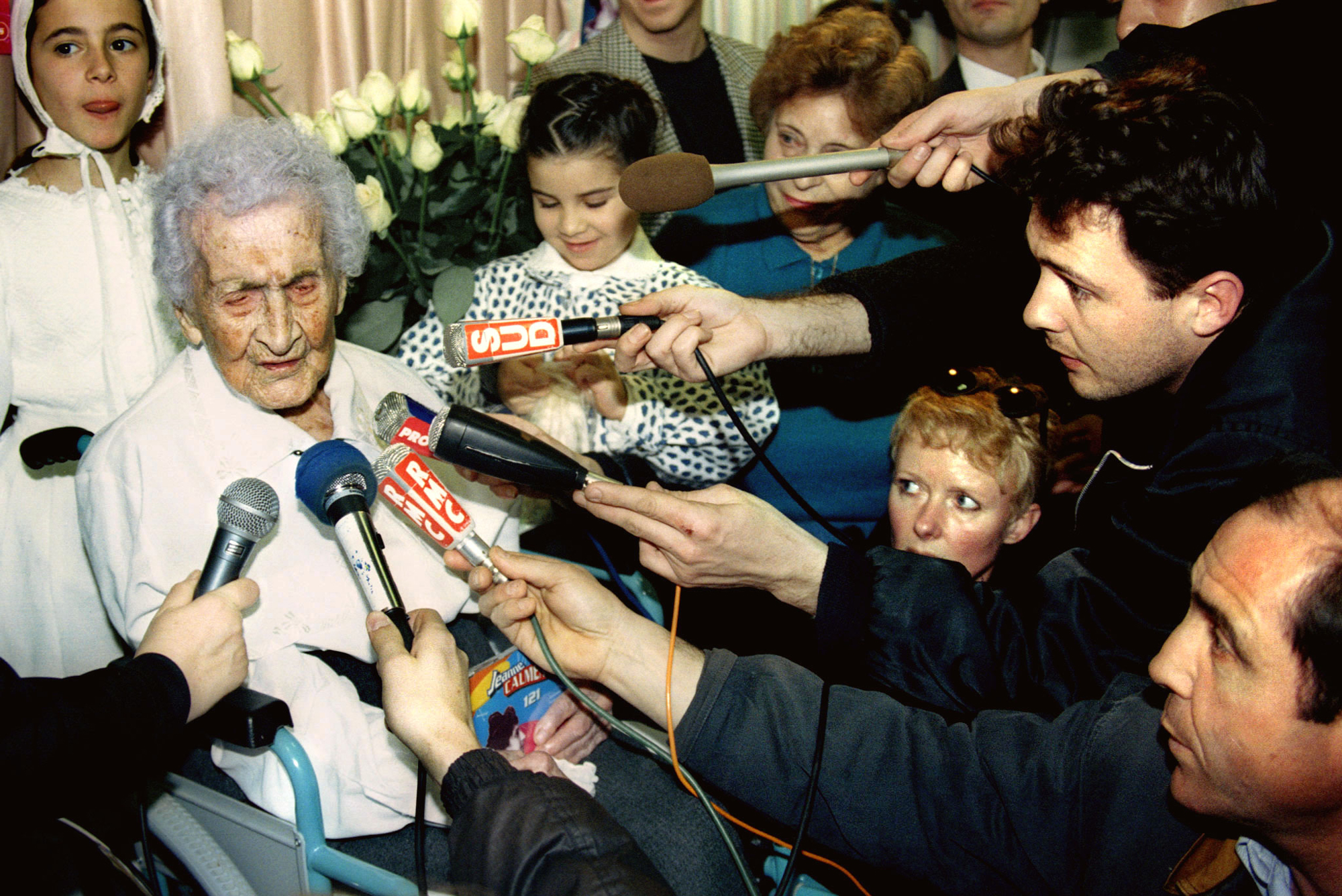 old white woman surrounded by reporters holding microphones