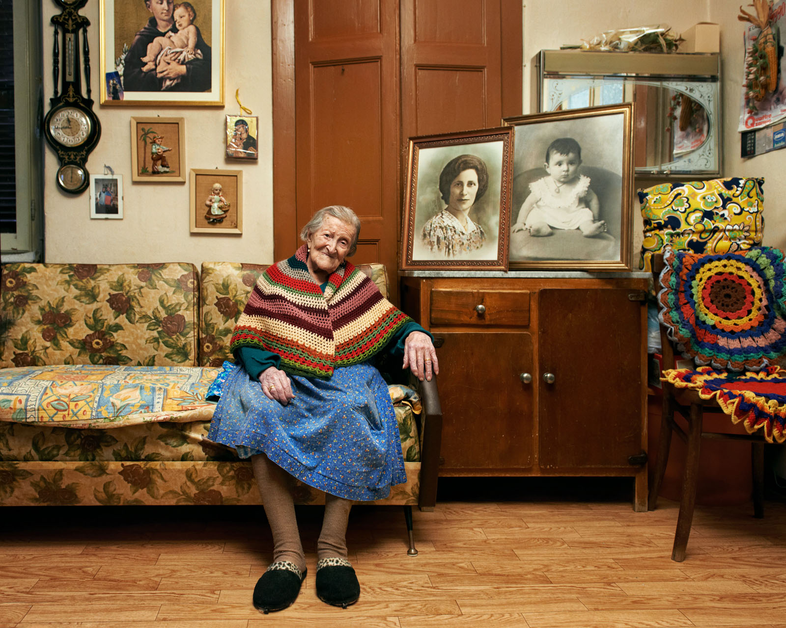 old smiling woman in knit shawl next to framed pictures of younger woman and baby