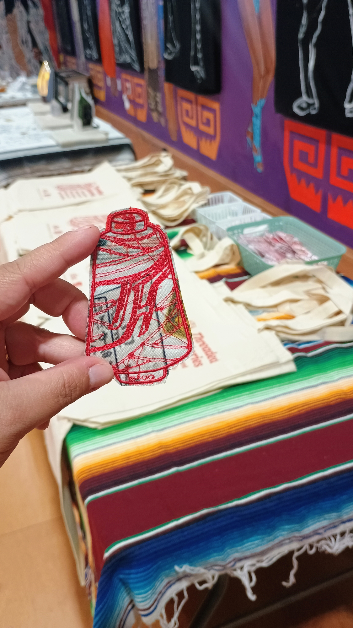 hand holding a red-sewn thread with a TH at the center