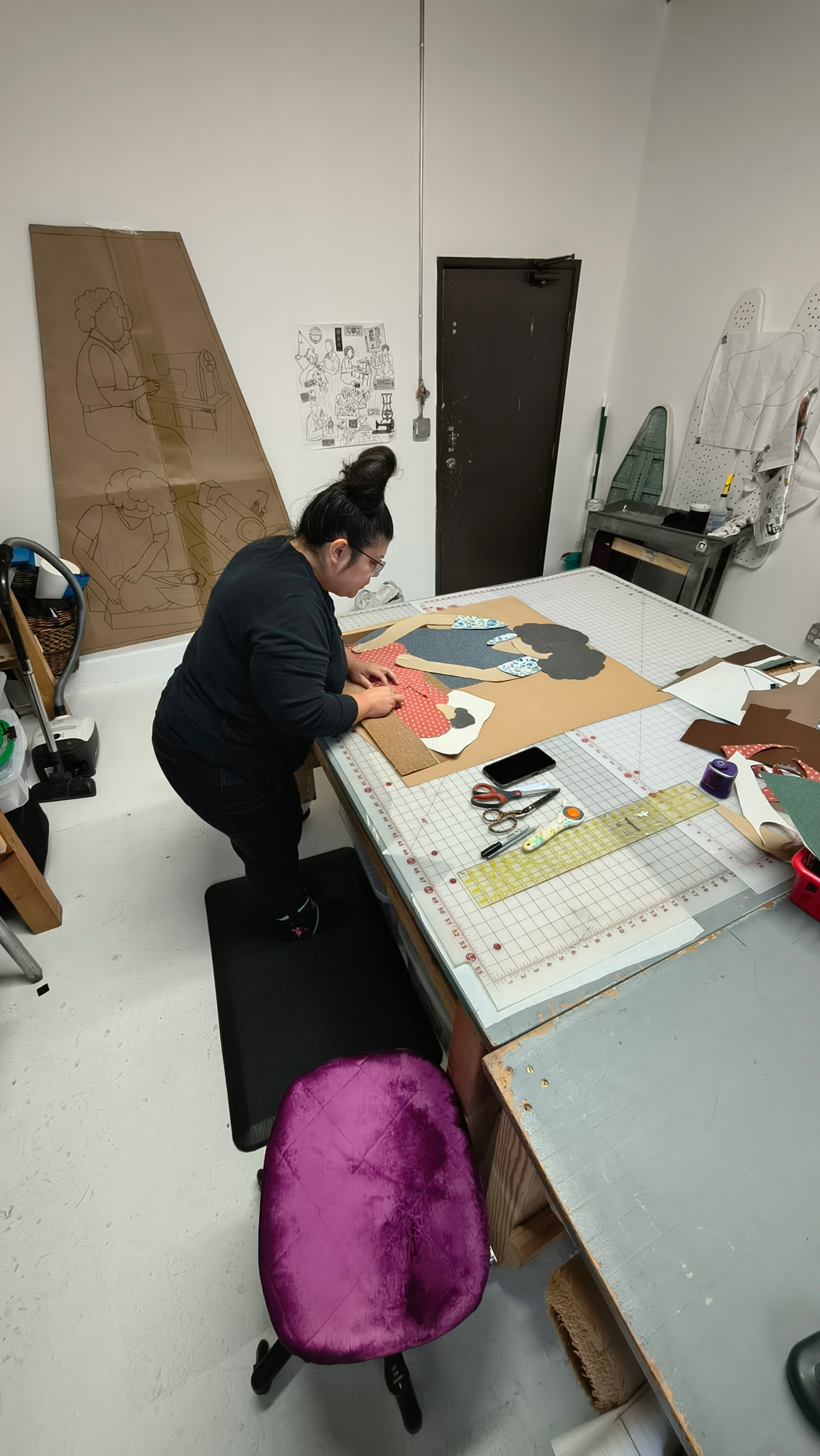 woman leans over sewing table working on large-scale design
